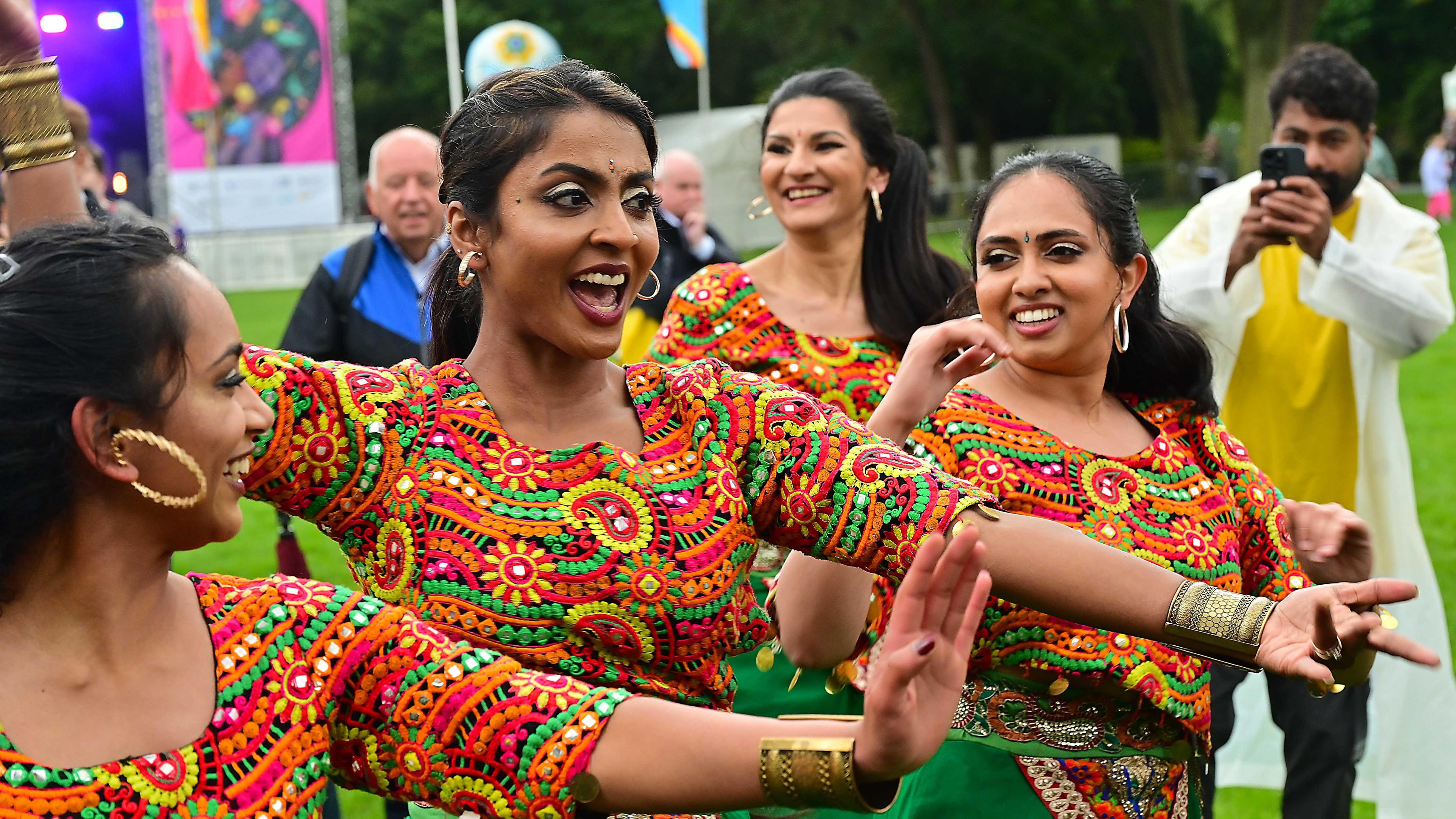 Three women with colourful neon patterned top smiling while dancing at the festival. 