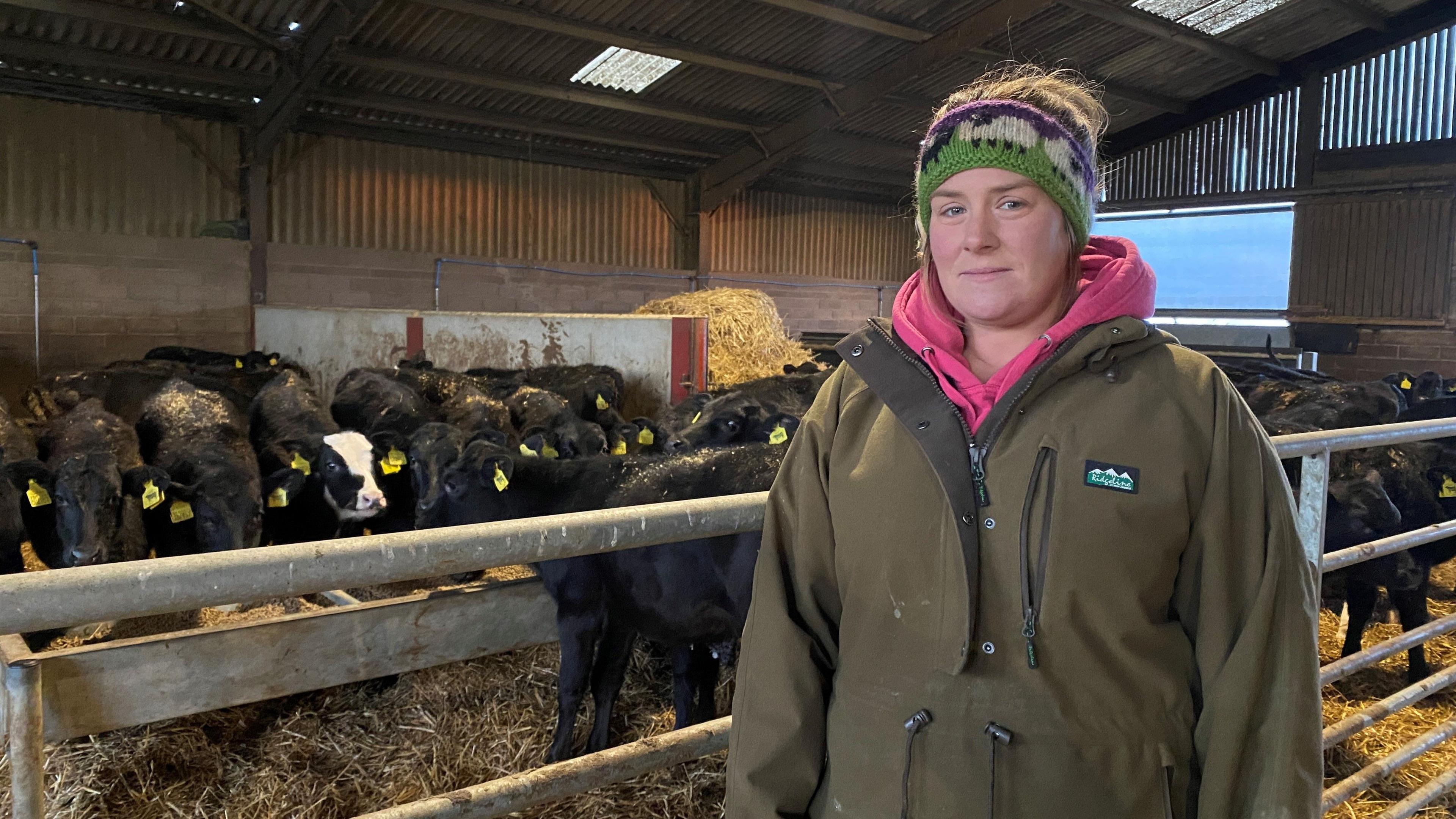 Rachel Fife is standing in front of some calves and is wearing a coat and a pink scarf.