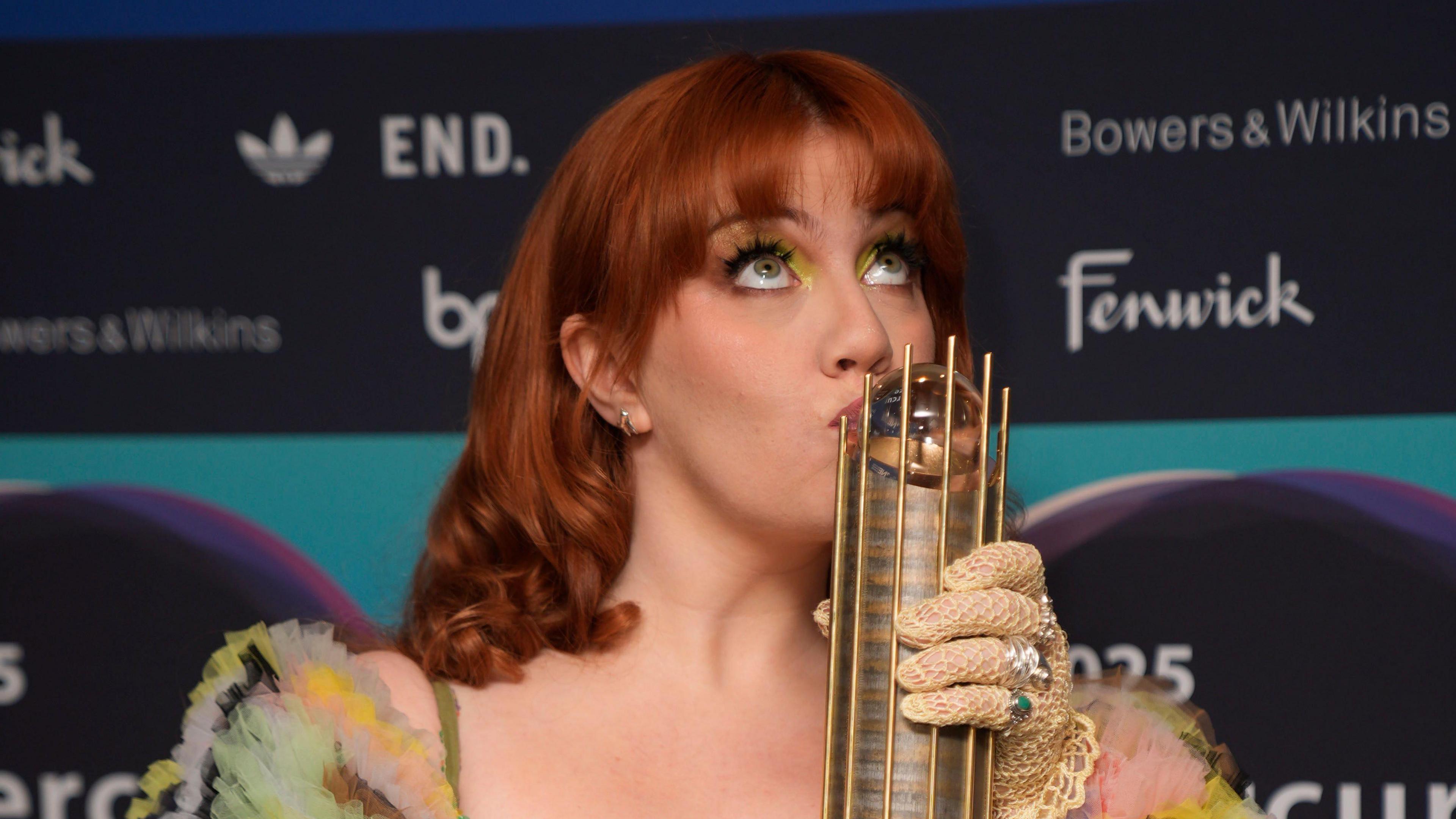 CMAT arriving for the 2025 Mercury Music Prize awards show, at the Utilita Arena, Newcastle. She is kissing her award for being nominated. She has red hair and green eyes and is looking up at the ceiling.