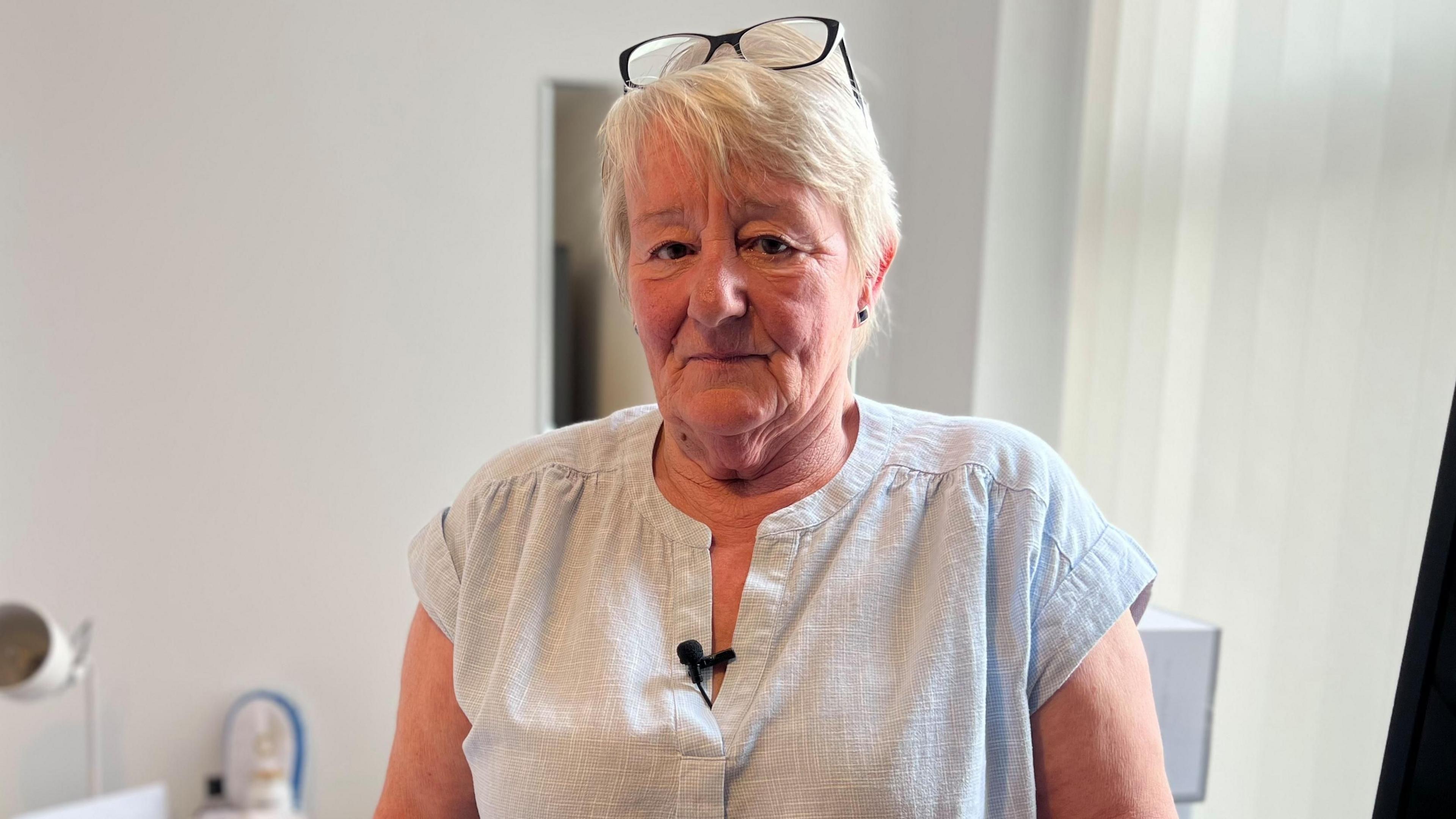 Woman with short blonde hair black glasses on head light blue blouse