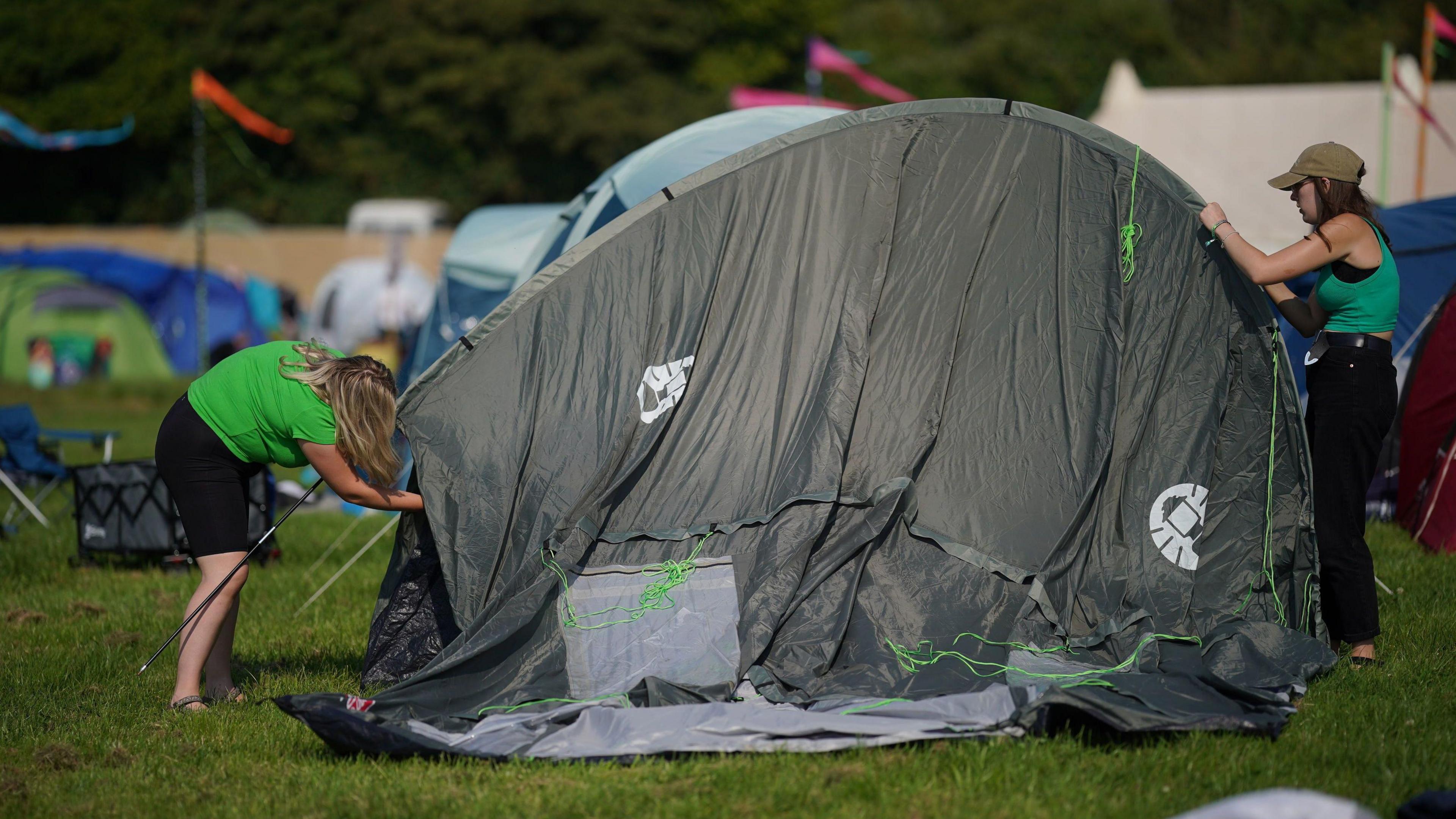 Two women set up a large grey tent at Glastonbury Festival. 