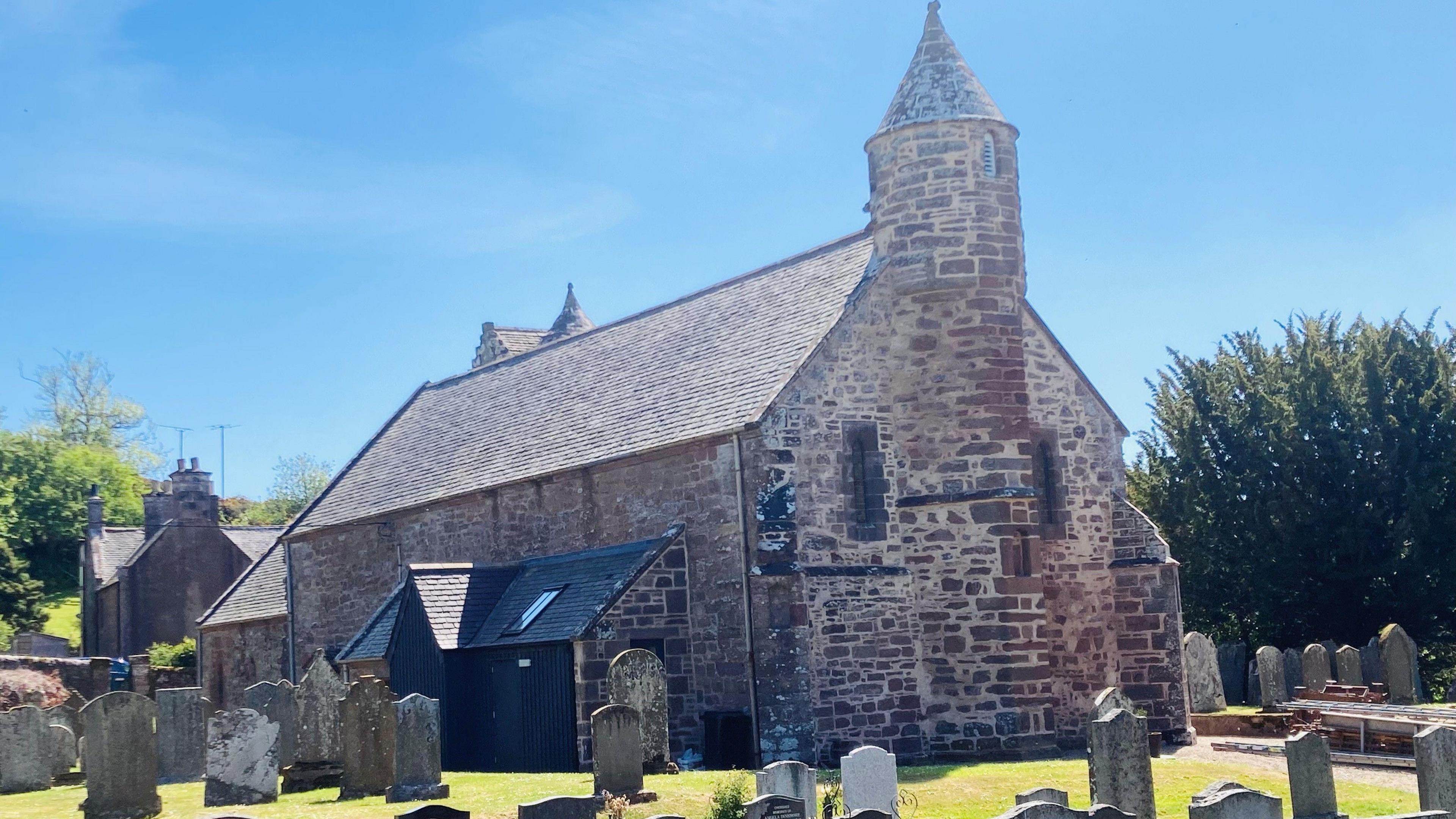 Church building - Arbuthnott Church - with graves in the foreground, under a blue sky.