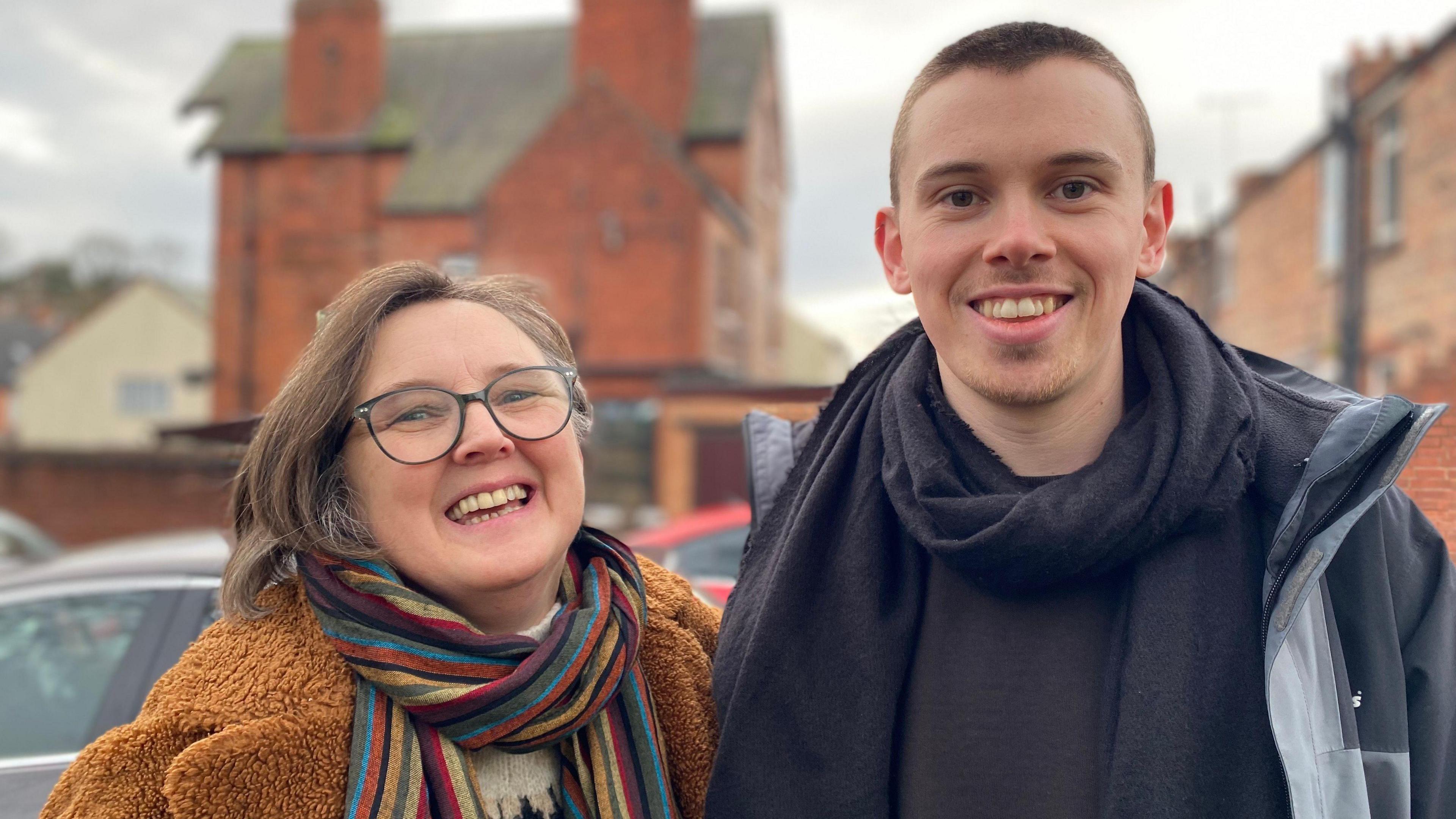 A woman with a multi-coloured scarf and a man with a black jumper and coat smiling.