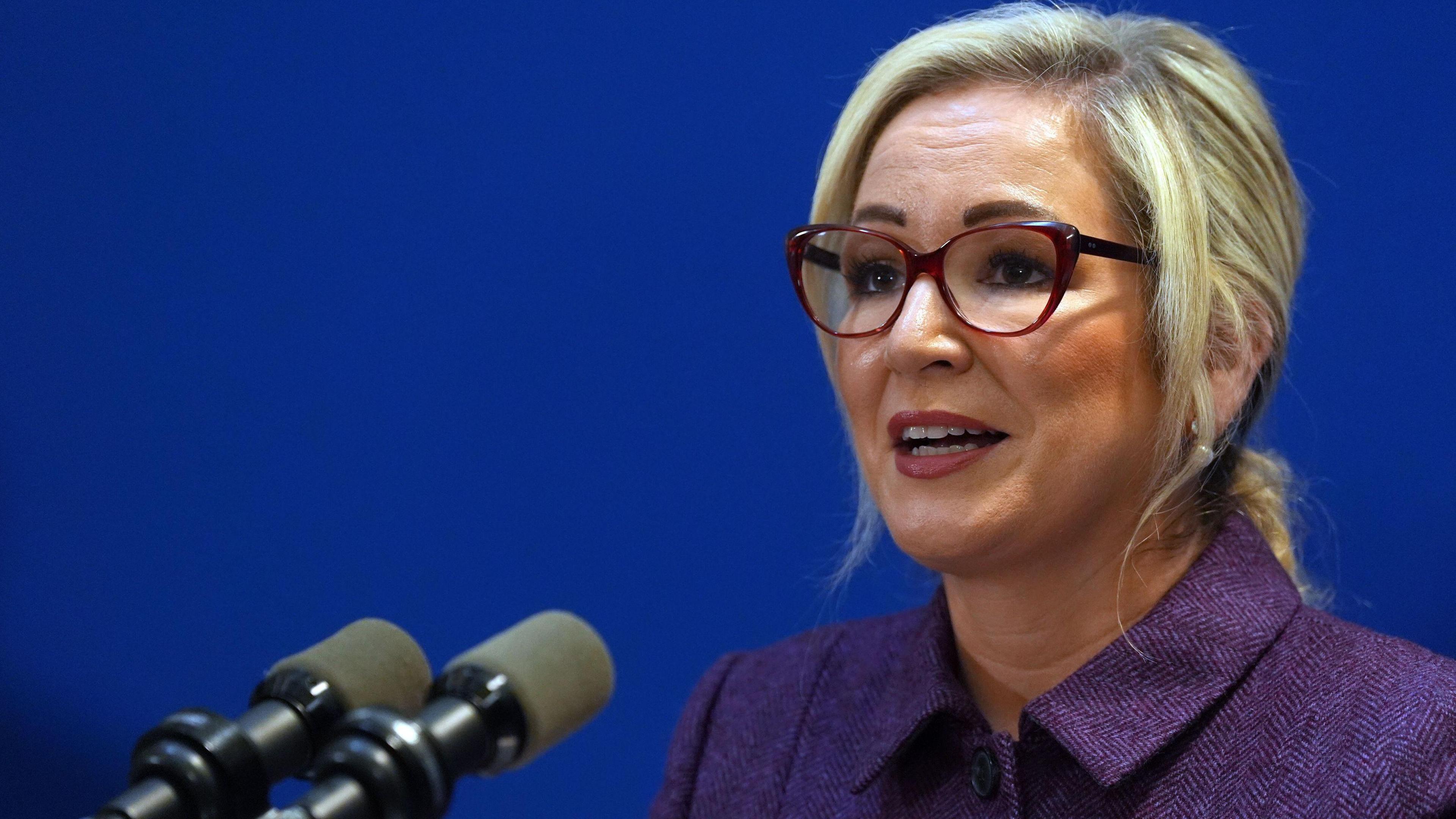 First Minister of Northern Ireland Michelle O'Neill speaks during a press conference, she is wearing a purple blazer and glasses. She has blonde hair.