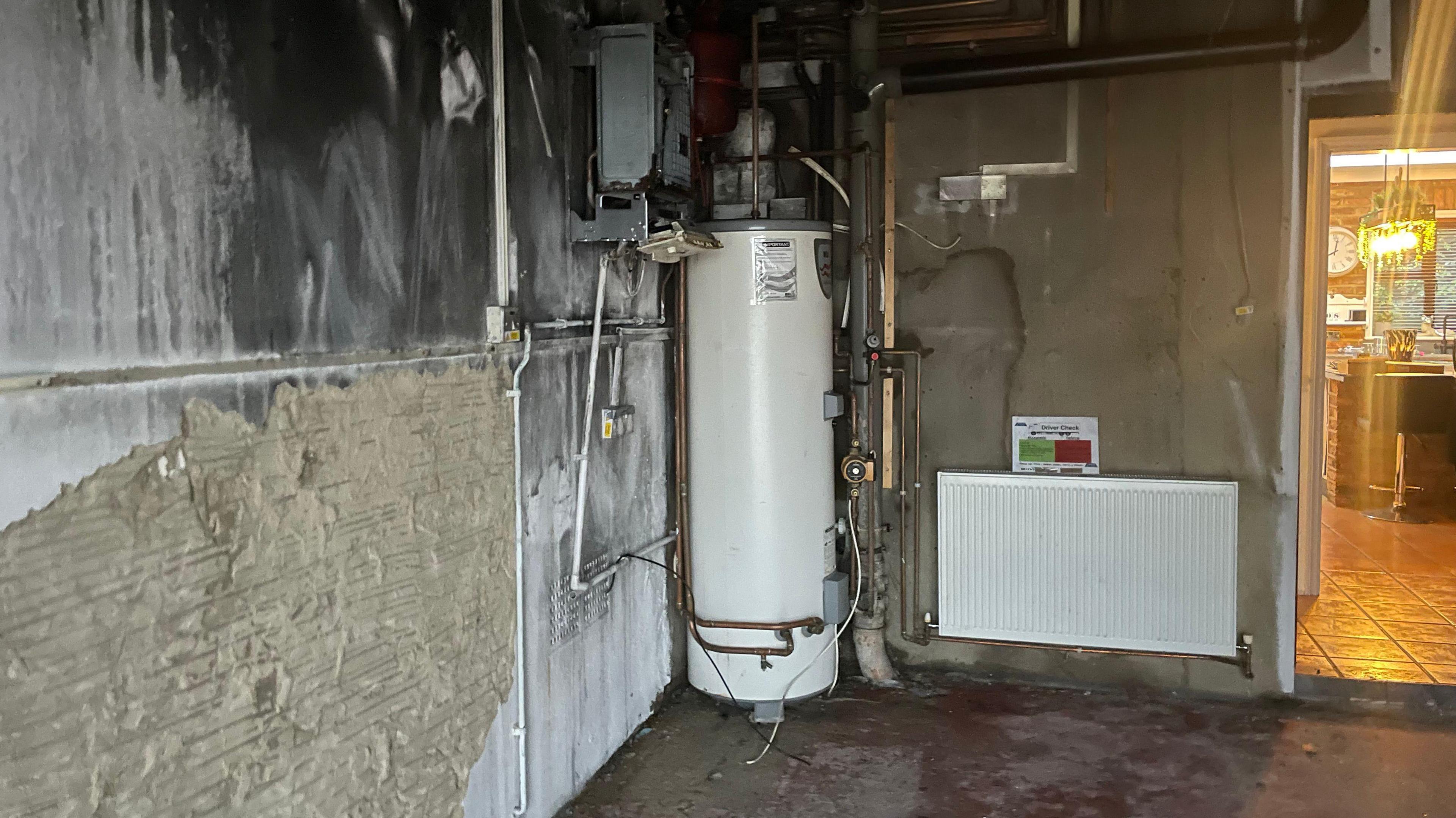 A boiler inside a damaged garage, which has soot on the wall.