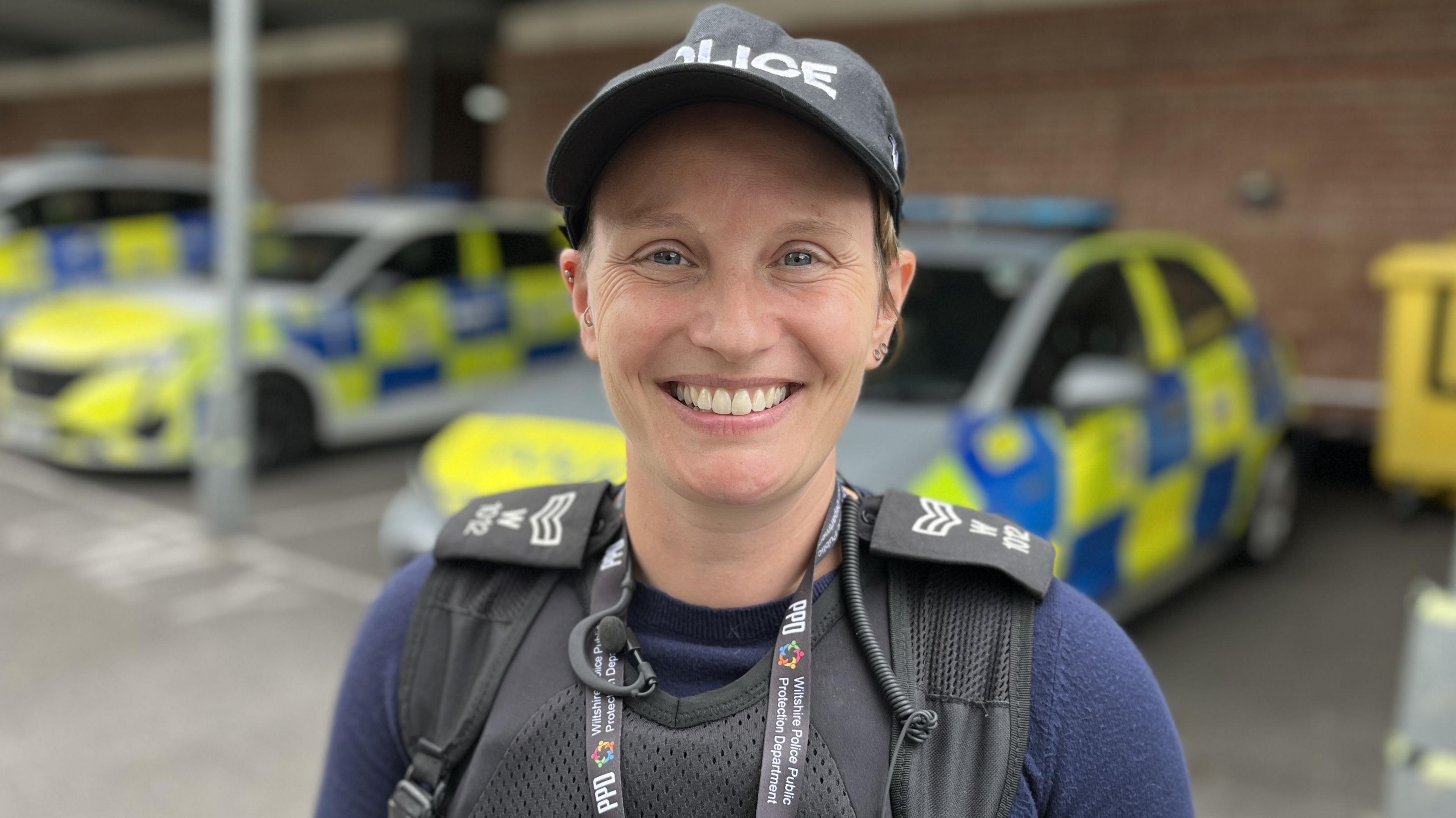 Detective Sergeant Jen Jeffcoat-Marsh smiling wearing a police baseball cap, stab vest and sergeant rank slides