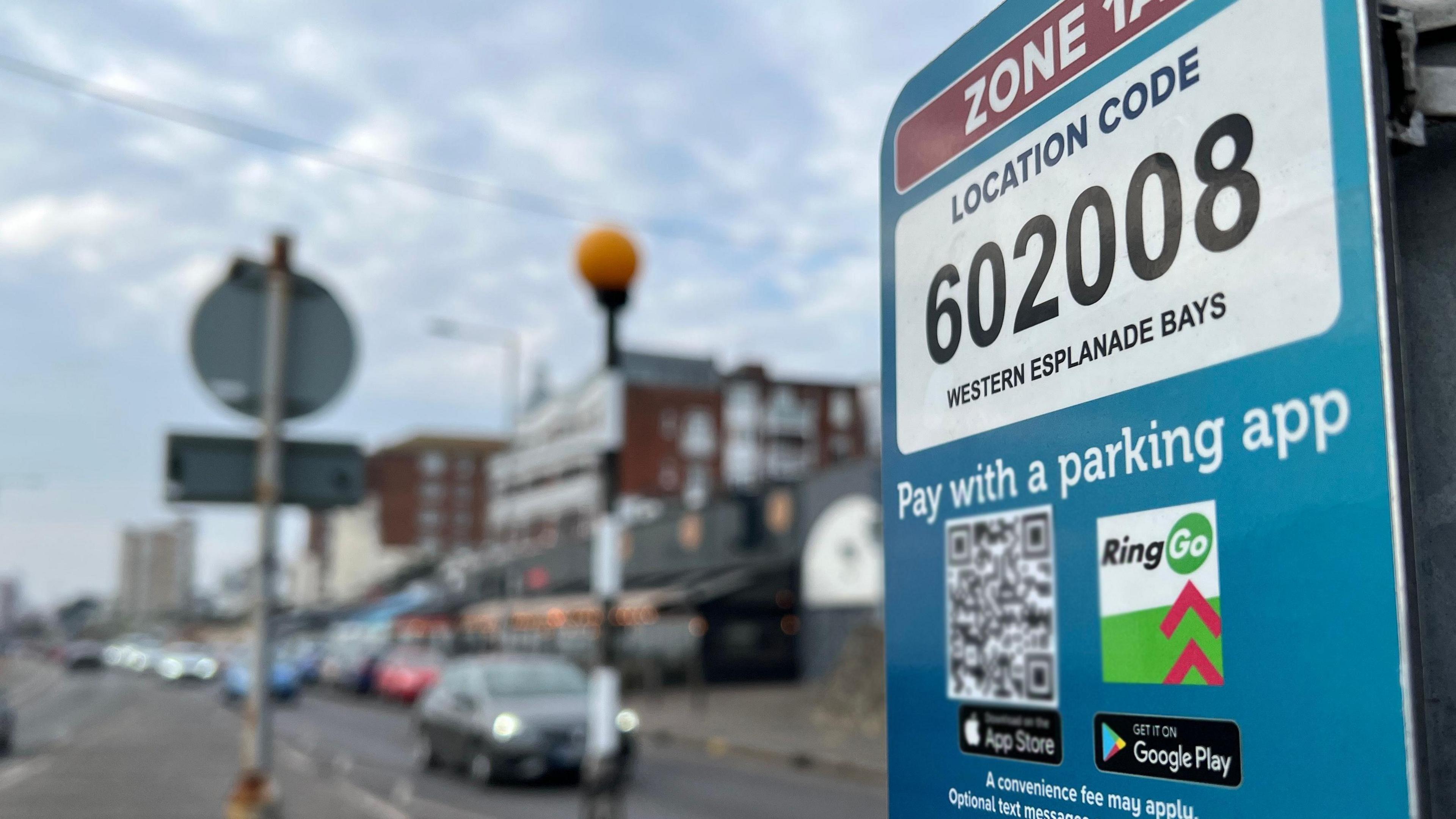 On the right is a sign which shows a pay with parking app, and different logos directing to places. In the background you can see a road in Southend. 