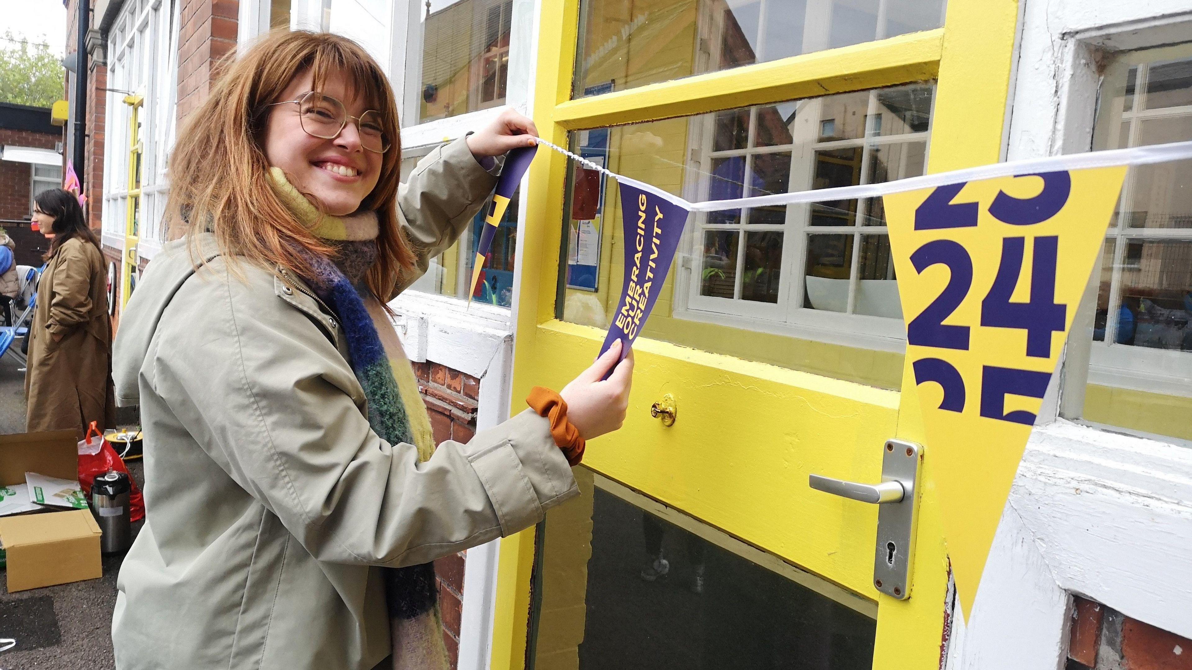 Event organiser smiling and hanging up flags wearing grey jacket