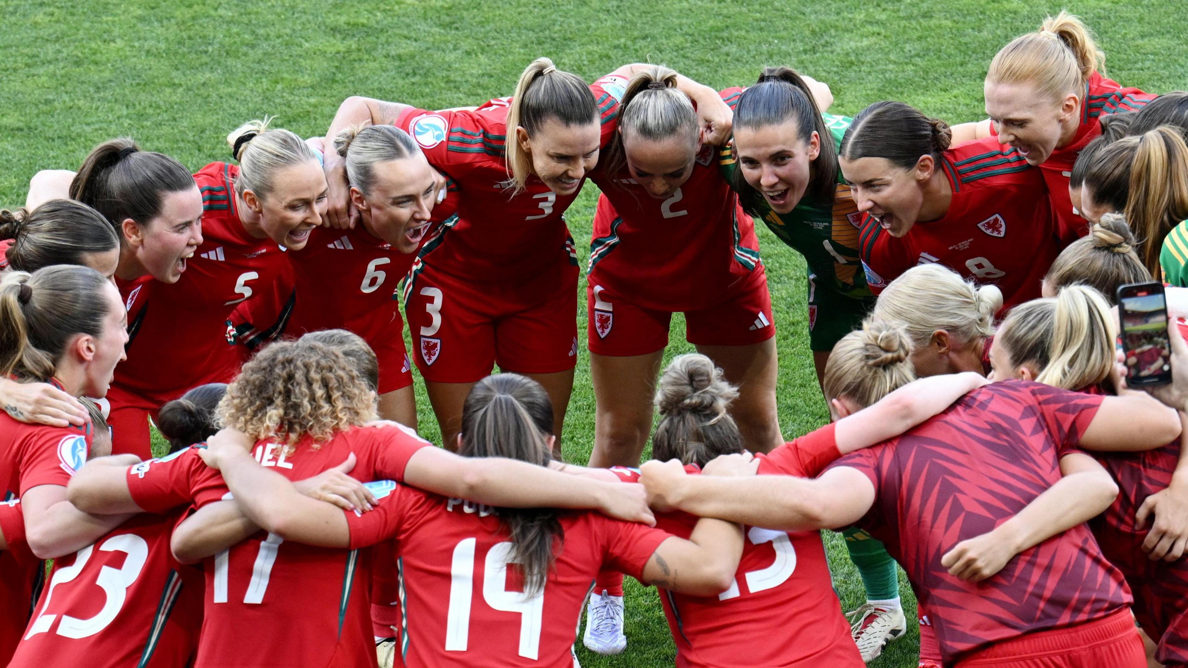 Welsh team huddled and smiling in their red kit.