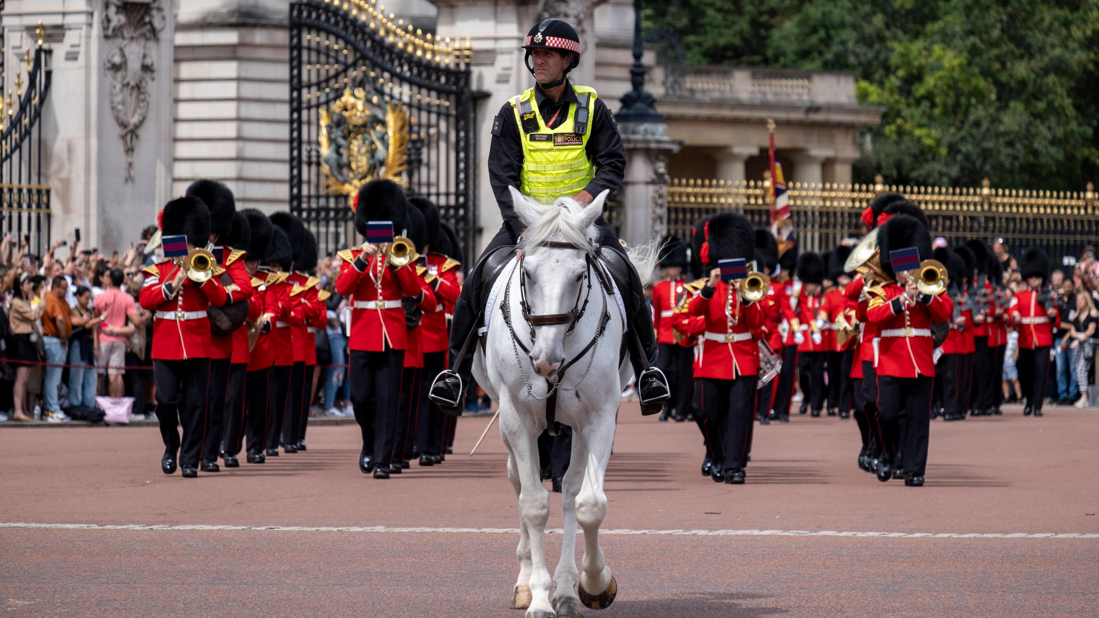 Tourists at Buckingham Palace watch in huge numbers as Changing of the Guard takes place. A police officer on a white horse rides before the march.