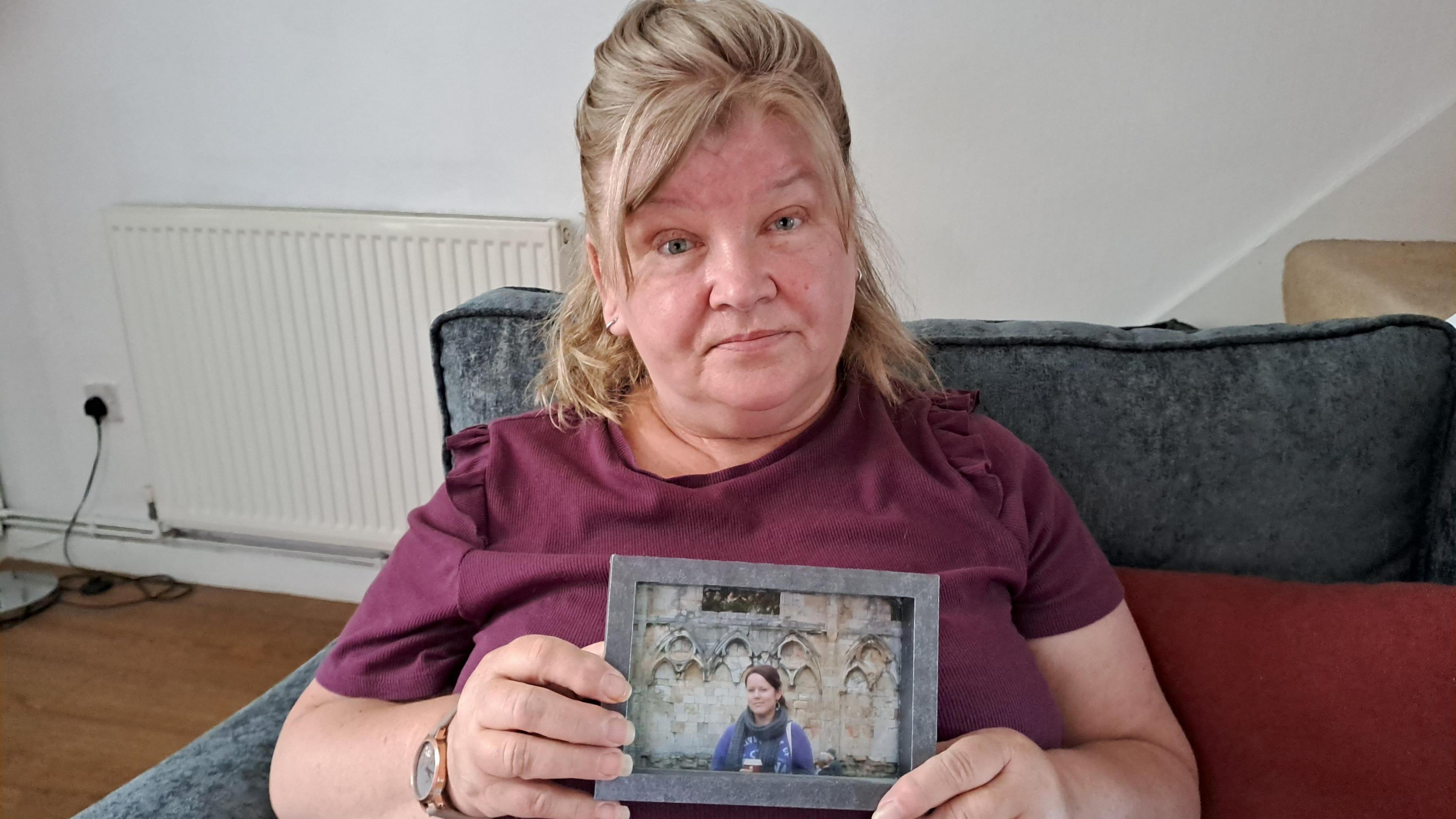 A woman in a maroon t-shirt holding up a picture of her daughter who died age 26