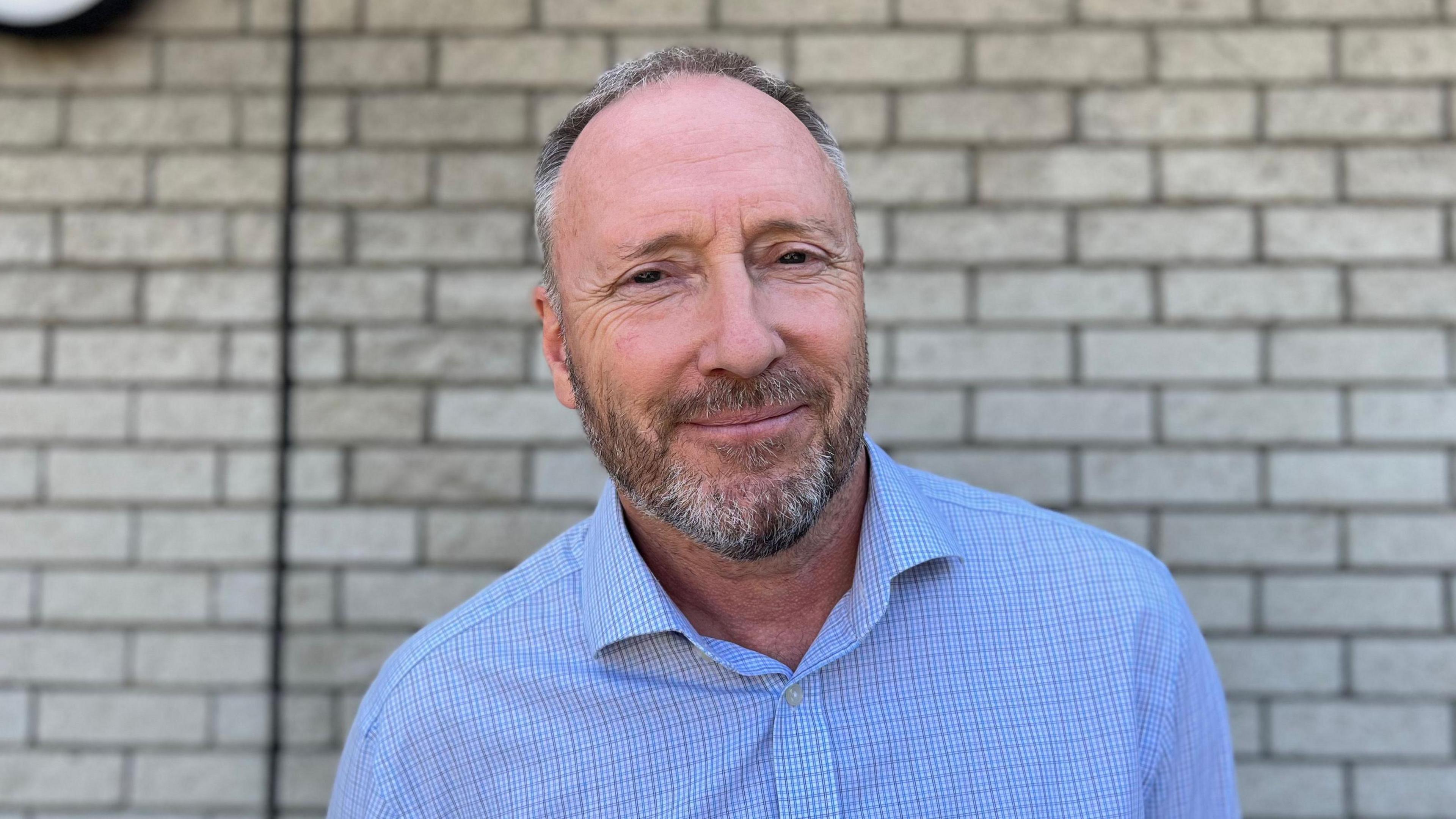 Deputy Paul Montague - A man with grey and black hair and a beard wearing a blue shirt.