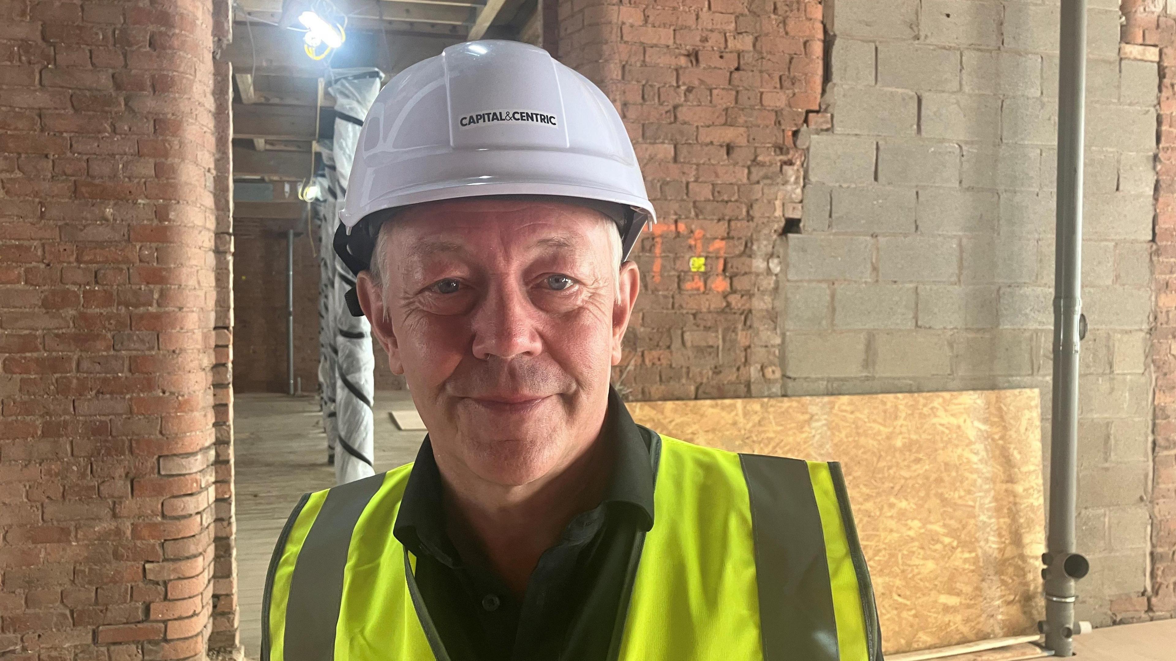 Photograph of the Manchester writer and tour guide Jonathan Schofield. He is pictured wearing a hard hat and a high-visibility jacket at Talbot Mill in Castlefield.