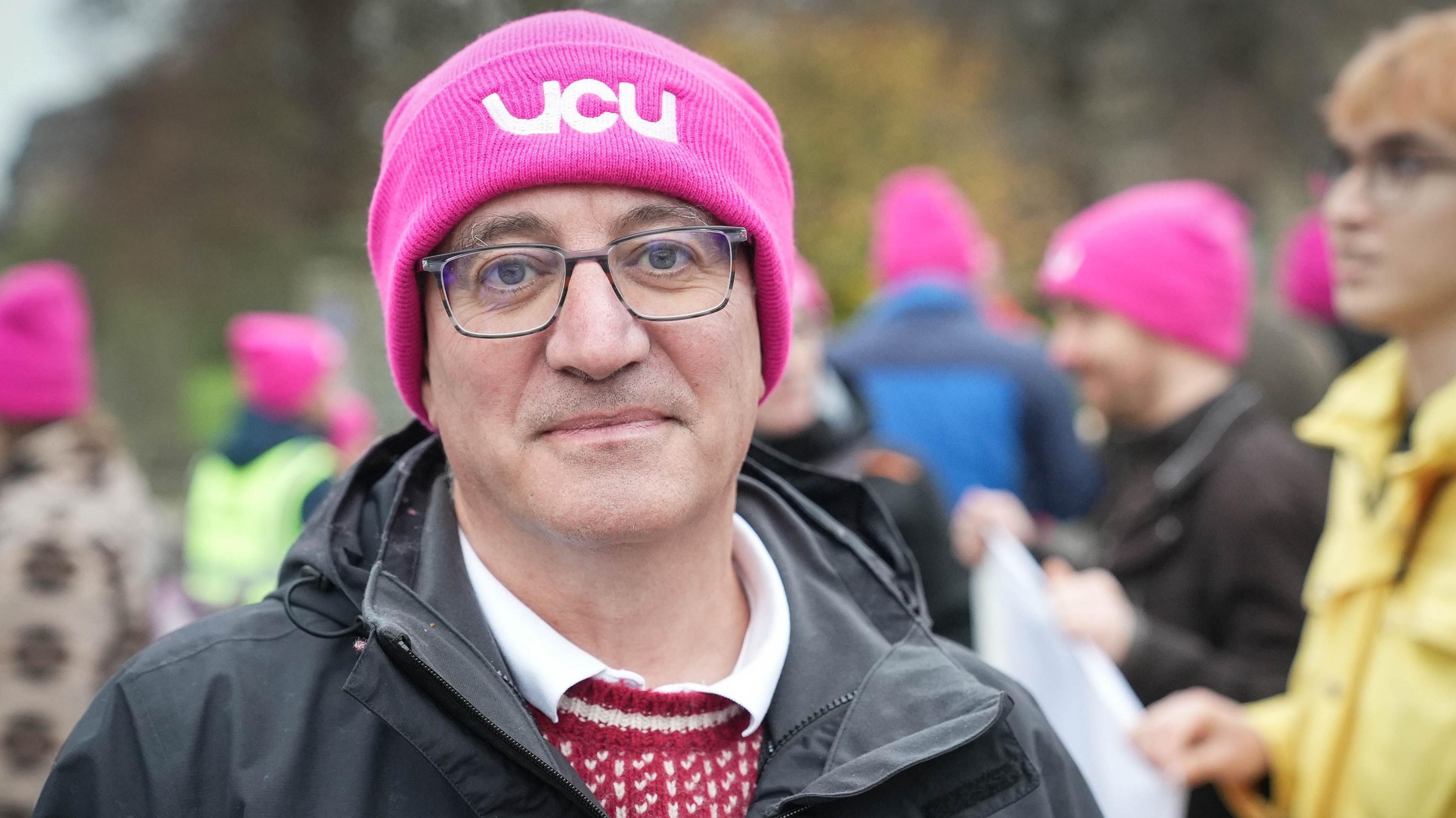 Carlo Morelli, a senior lecturer in economics at the University of Dundee, wearing a pink UCU hat while standing on a picket line with other union members in the background.