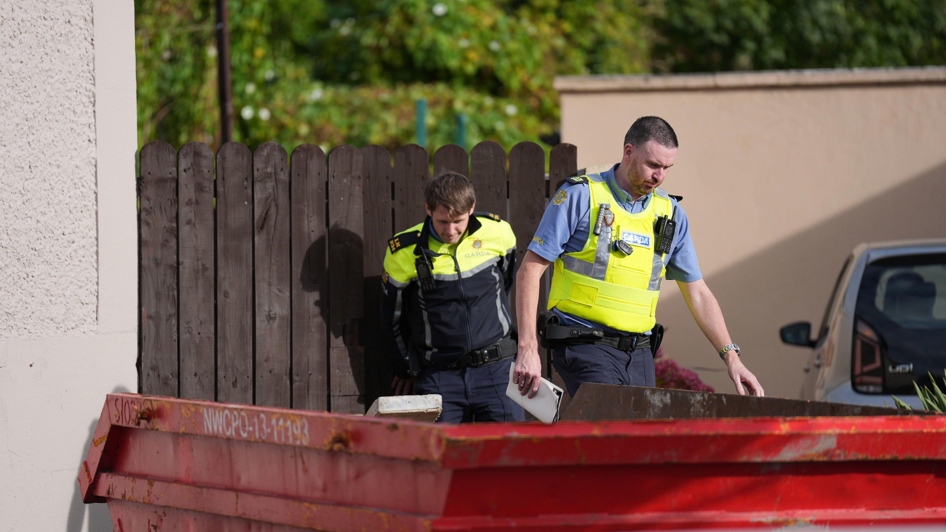 Two uniformed male garda officers on duty during the search for Kyran Durnin in Dundalk.   A red metal skip is pictured in foreground. 