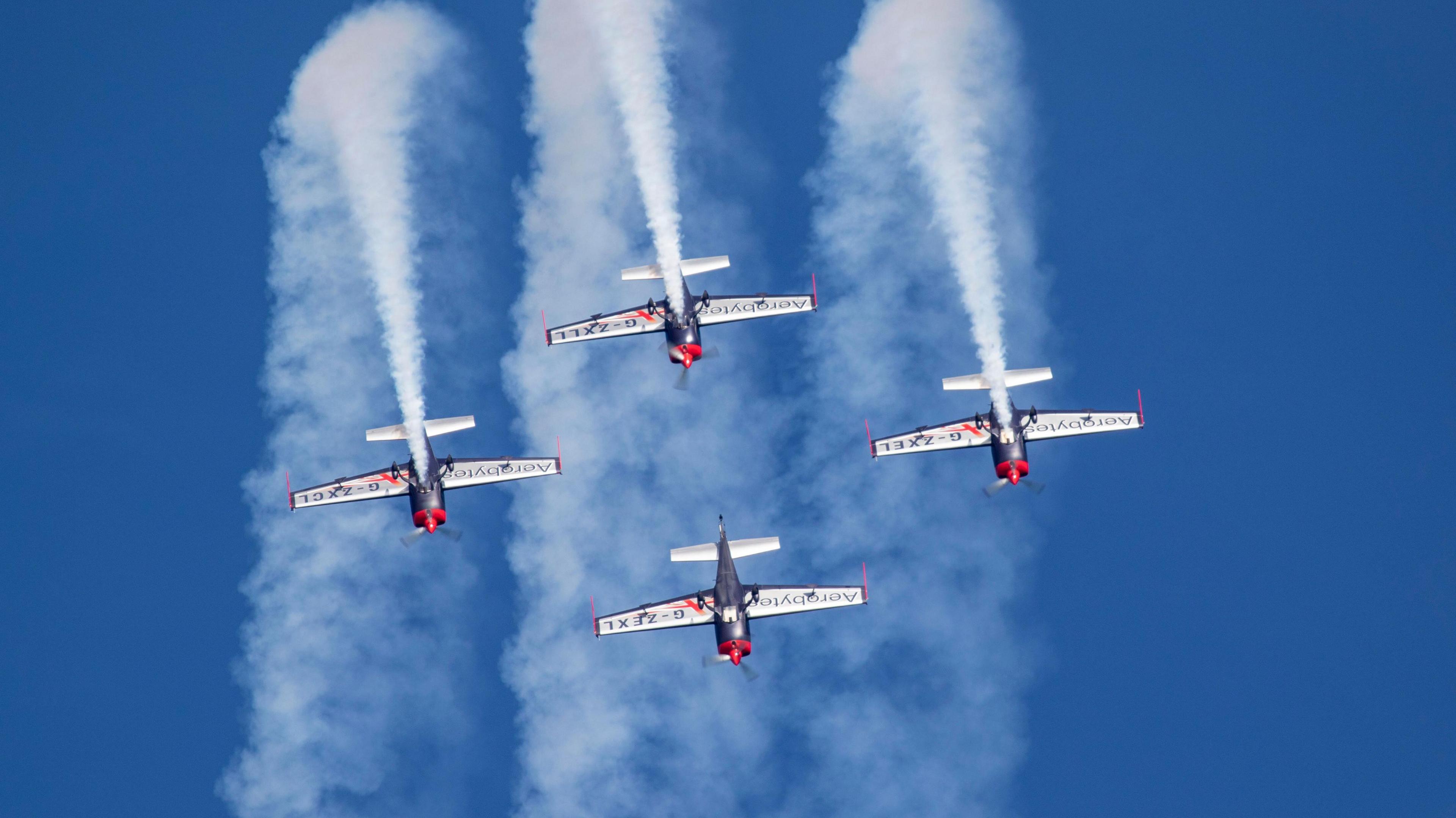 Four red, blue and white aircraft during a display amidst blue skies.