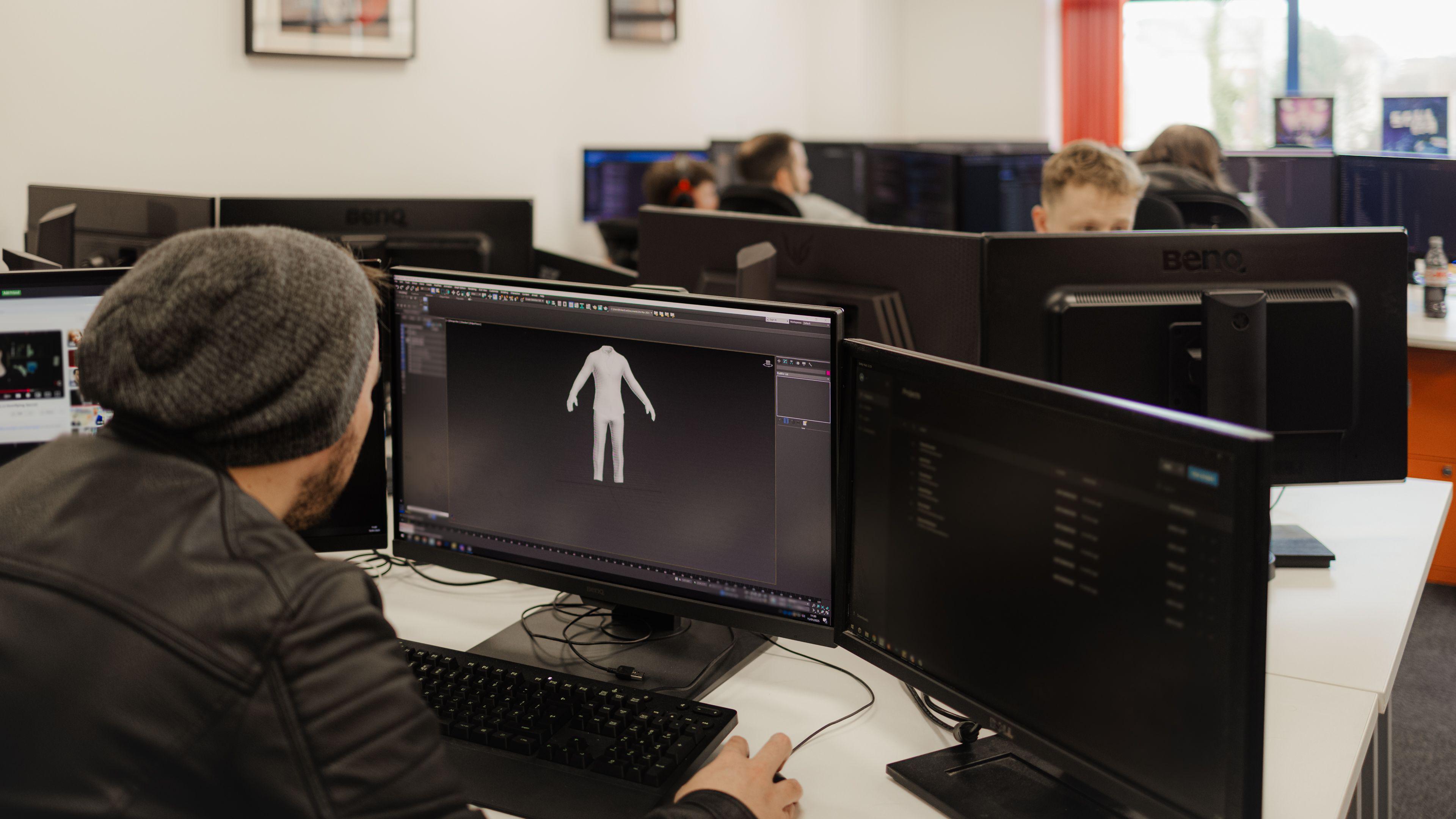 A man working at a PC is designing a character for a video game, with a 3D model of the character appearing on the screen in front of him.