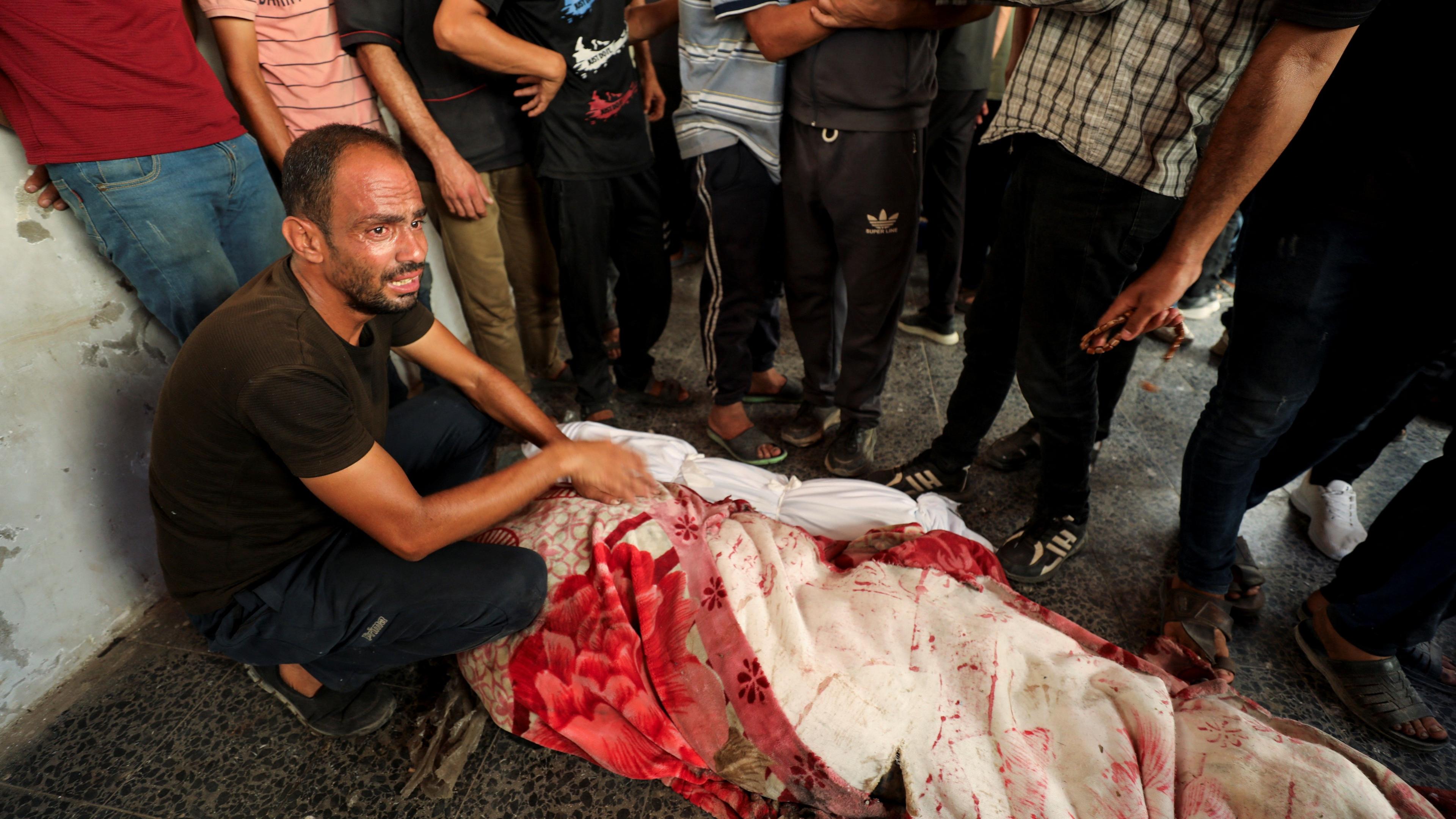 A Palestinian man next to a body wrapped in sheets, after a school that was sheltering displaced people was hit by an Israeli strike, amid the Israel-Hamas conflict, at a hospital in Gaza City.