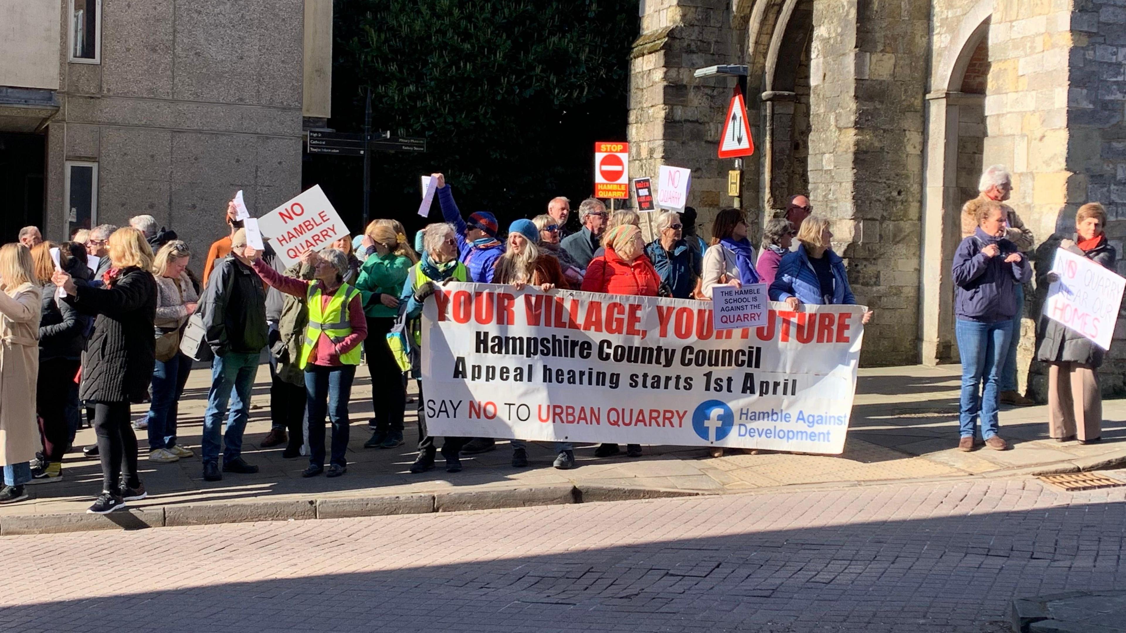 People of all ages with signs stood along a pavement protesting.