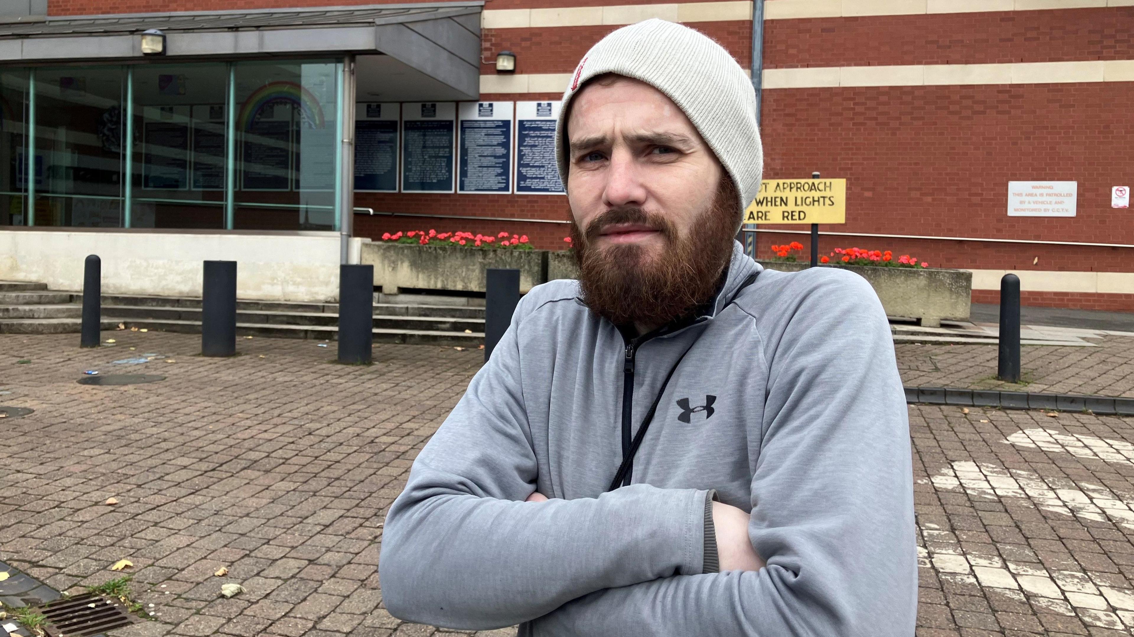 Released prisoner Ryan Surplice stands outside HMP Manchester with his arms folded in a grey top wearing a beanie. 