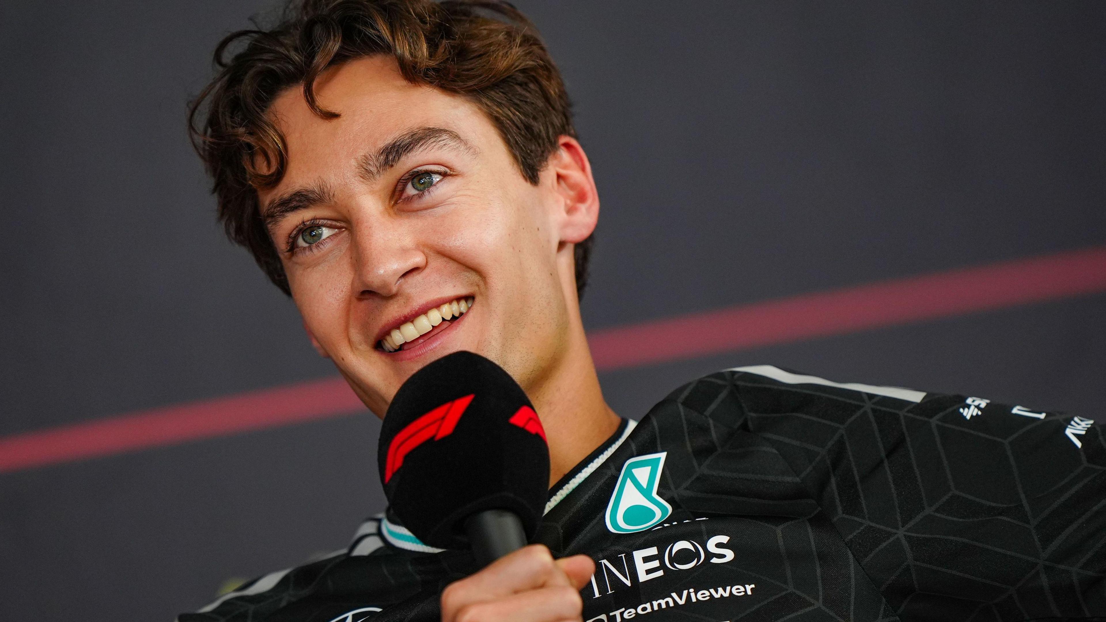 A smiling George Russell speaking into an F1-branded microphone during a news conference at Bahrain testing