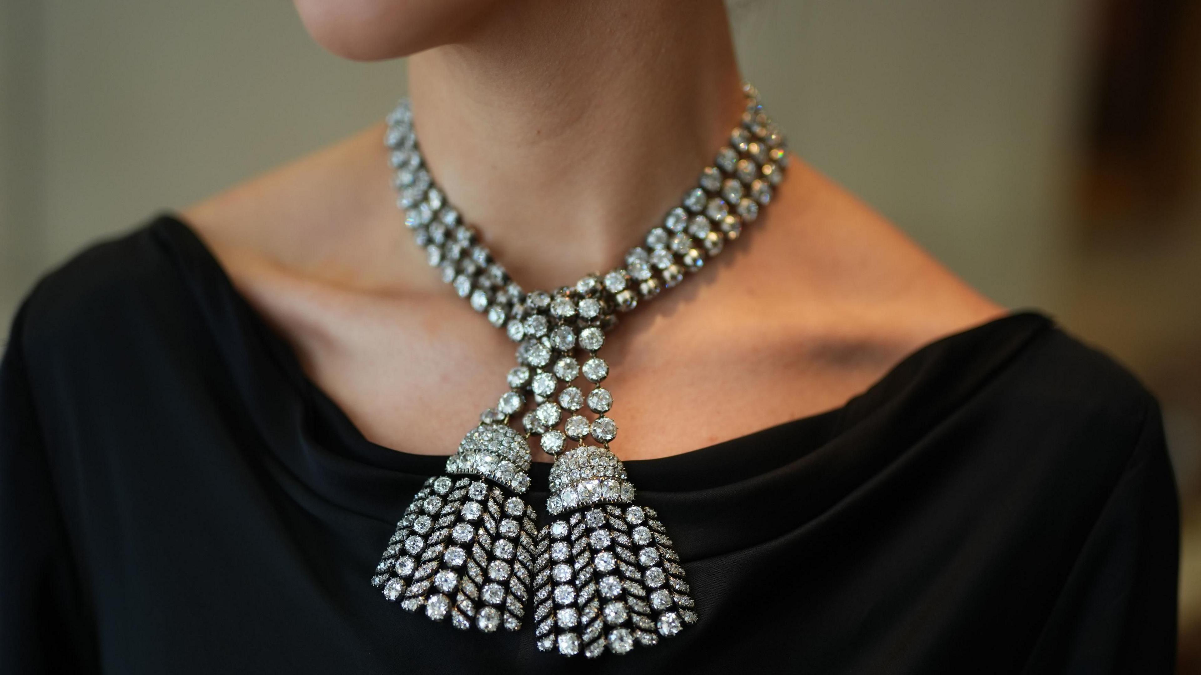 The diamond necklace is formed of two tassels and rest on the neck and black t-shirt of an anonymous wearer. 