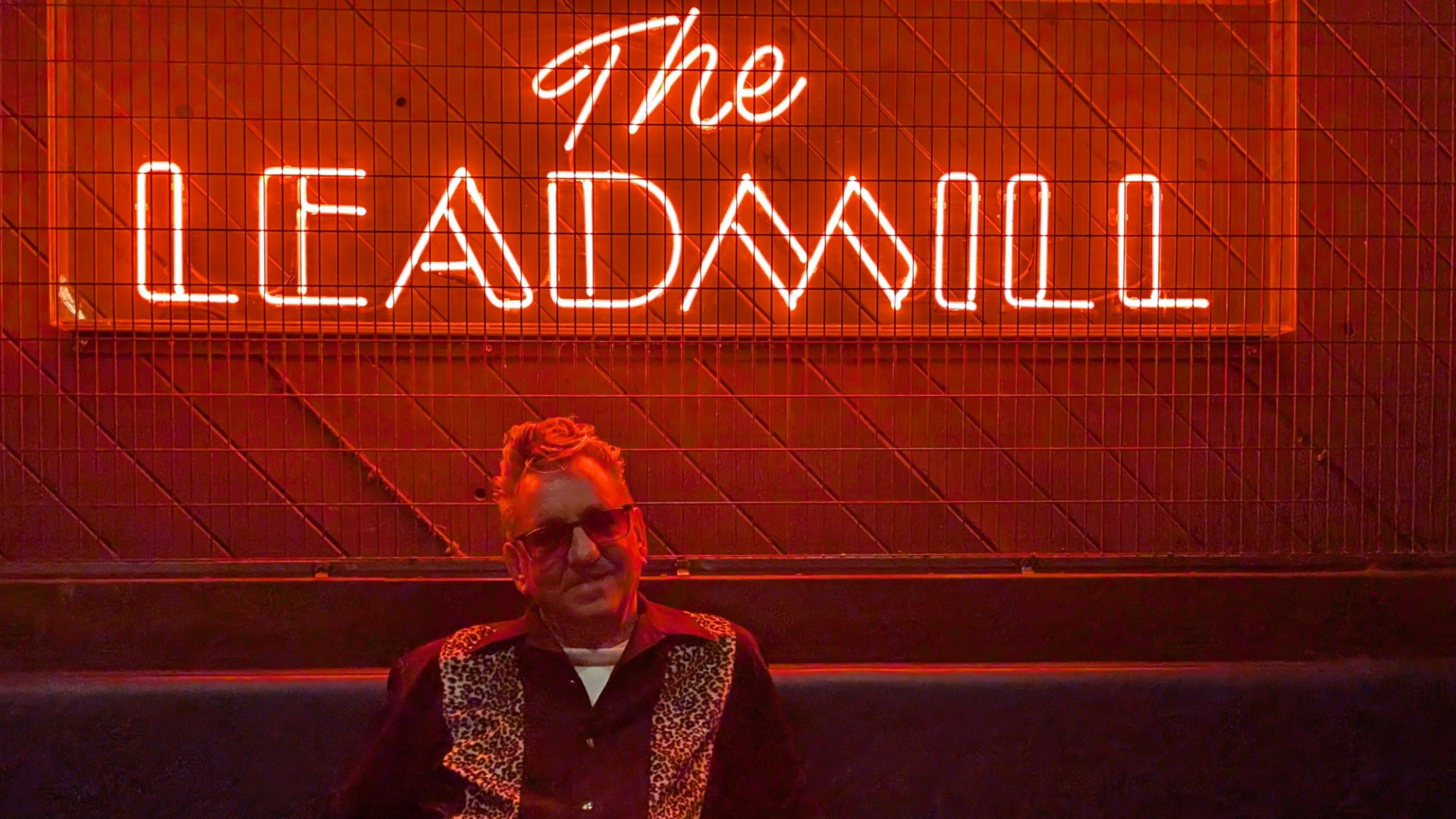 Richard Hawley sat under a red neon light which reads 'The Leadmill'