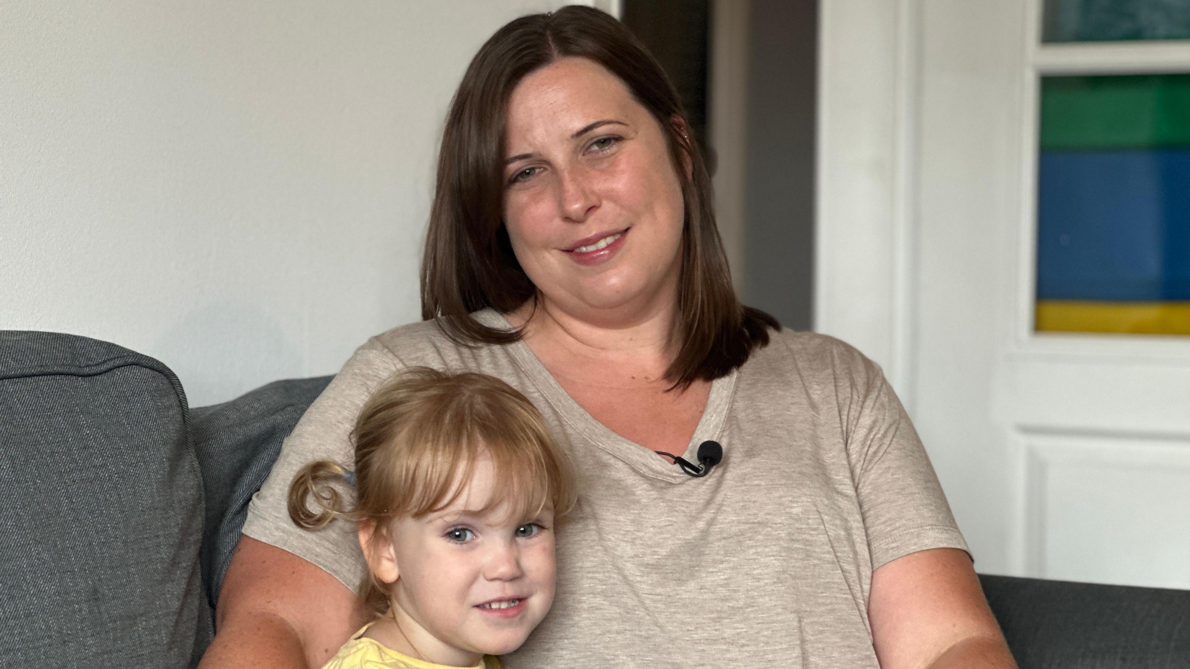 A woman and a child, Susie and Alice, sitting on a grey sofa with white walls and door behind.