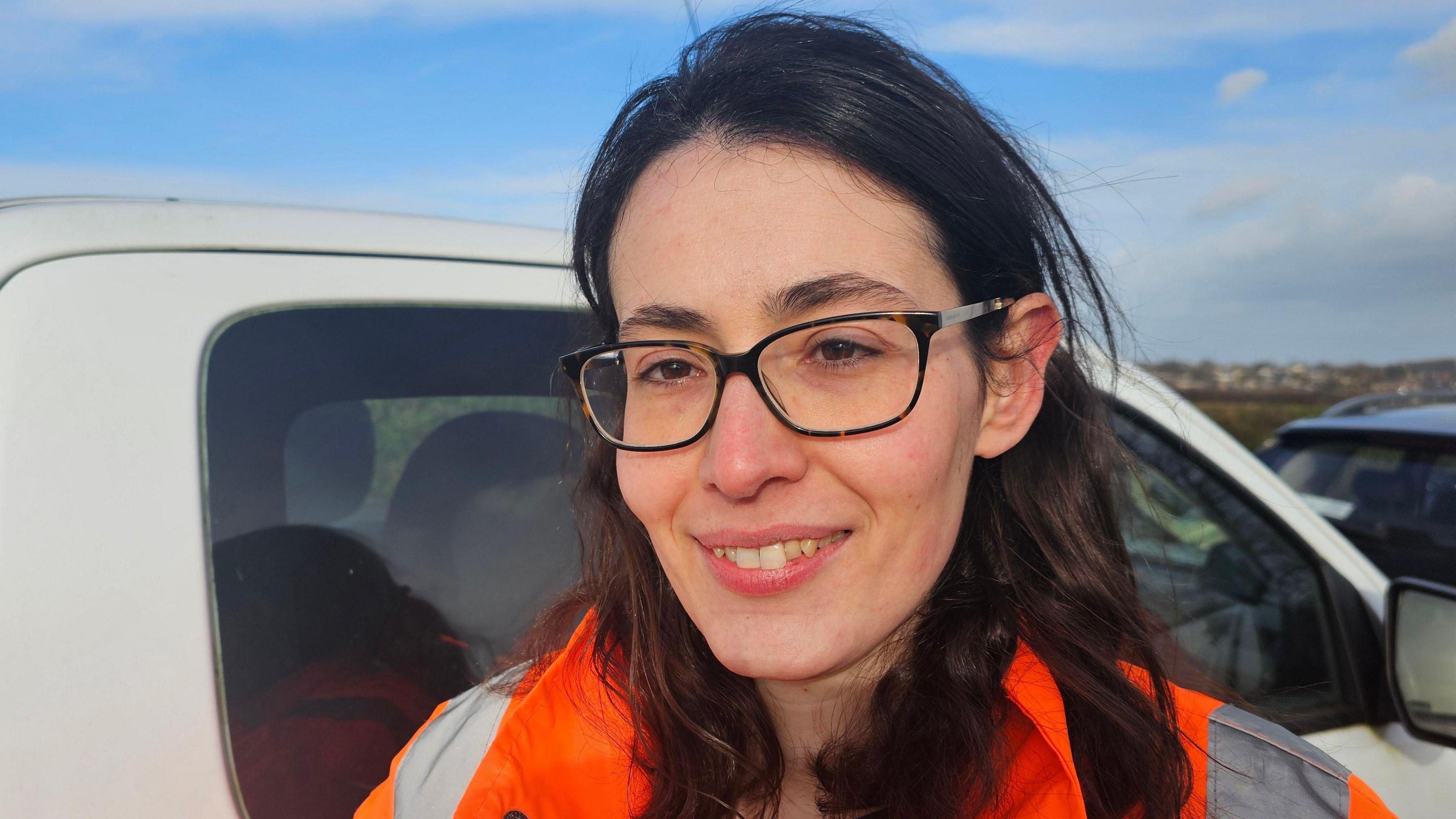 Head and shoulders picture of Charlotte Cupit, smiling and wearing an orange high-vis jacket in front of a white vehicle