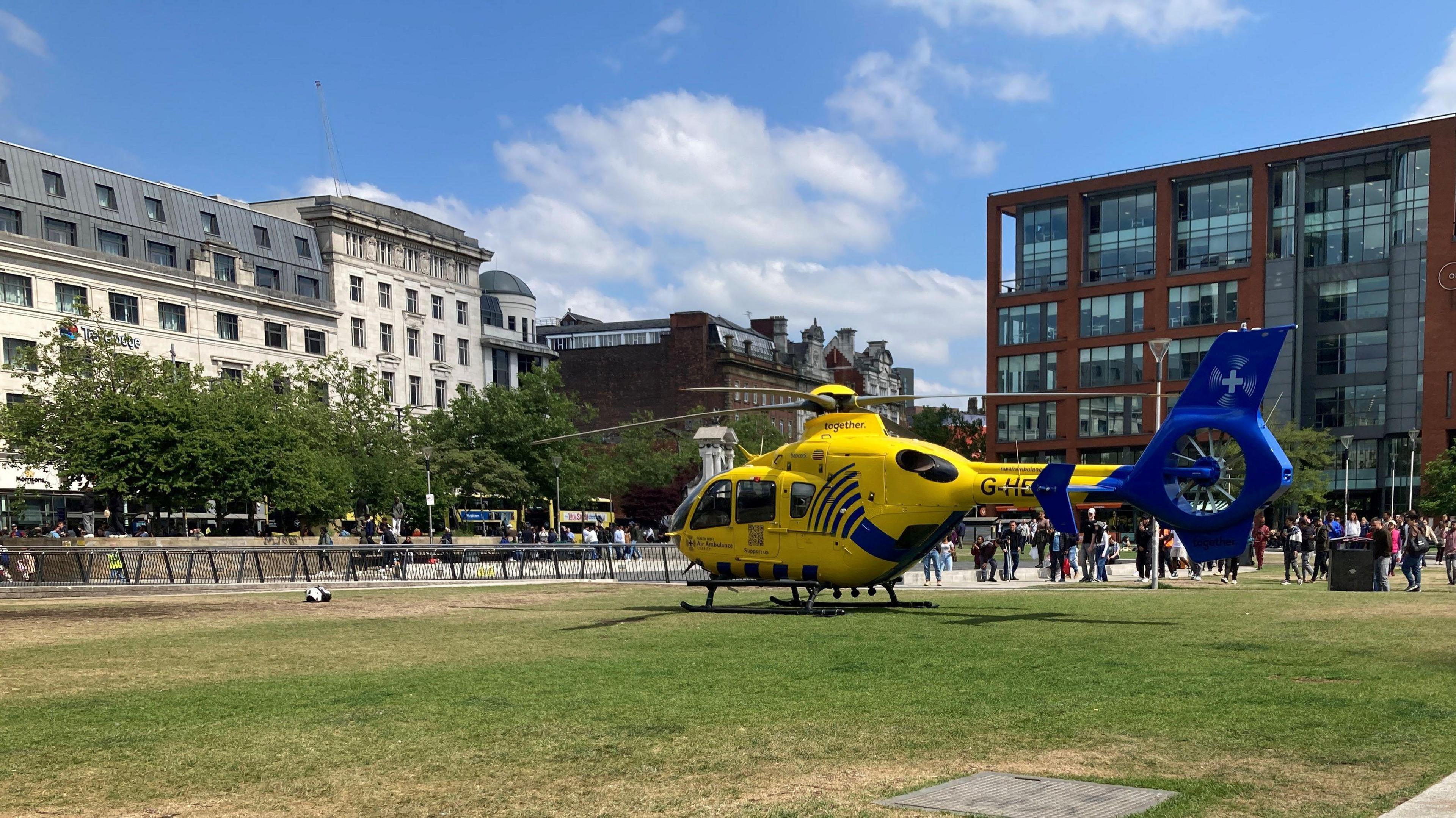 The yelow and blue air ambulance in the middle of Piccadilly Gardens, on the grass