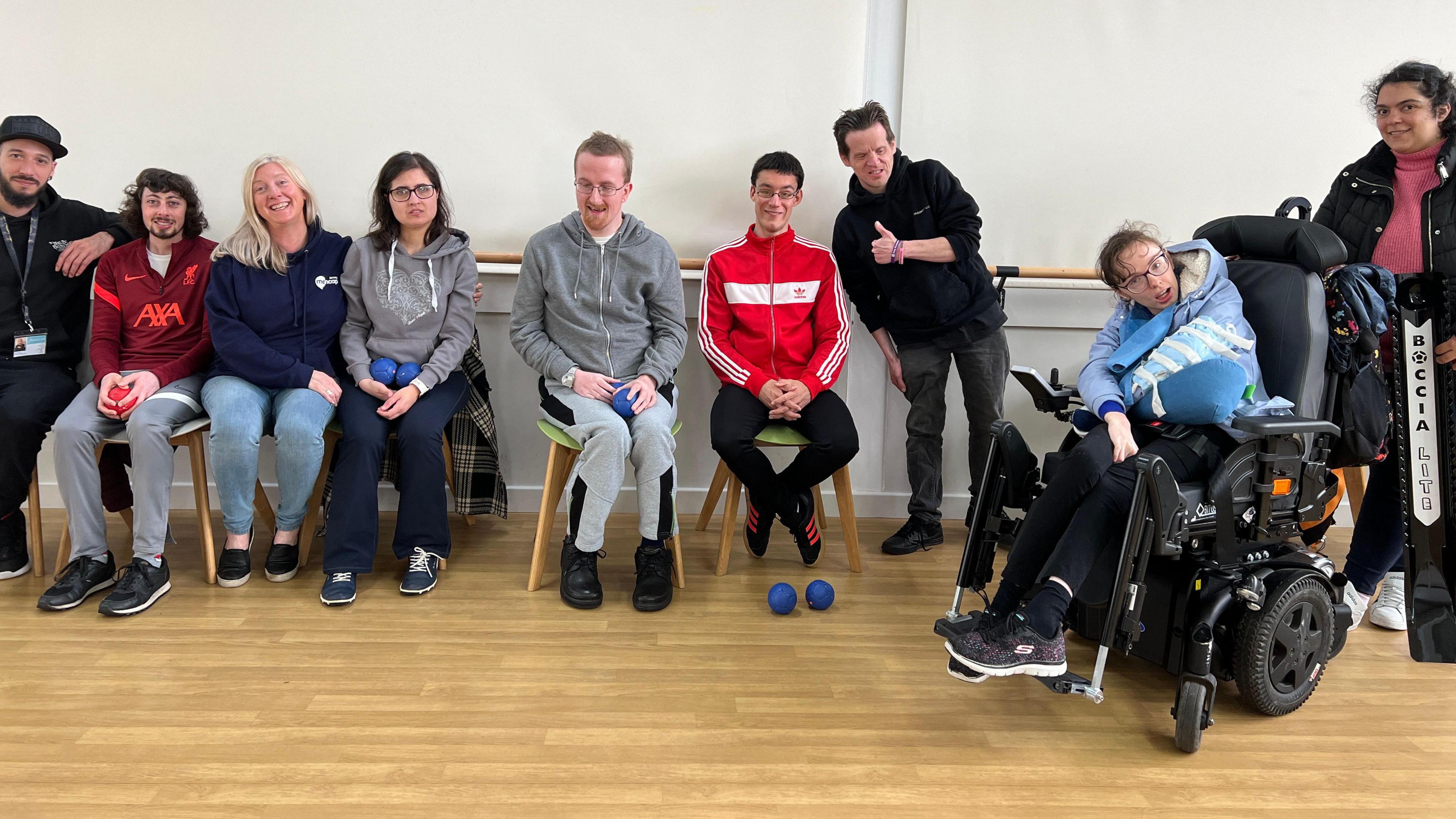 Members of Jersey Mencap smile at the camera and most are sat down in chairs with bowls on their laps for a game of indoor bowls