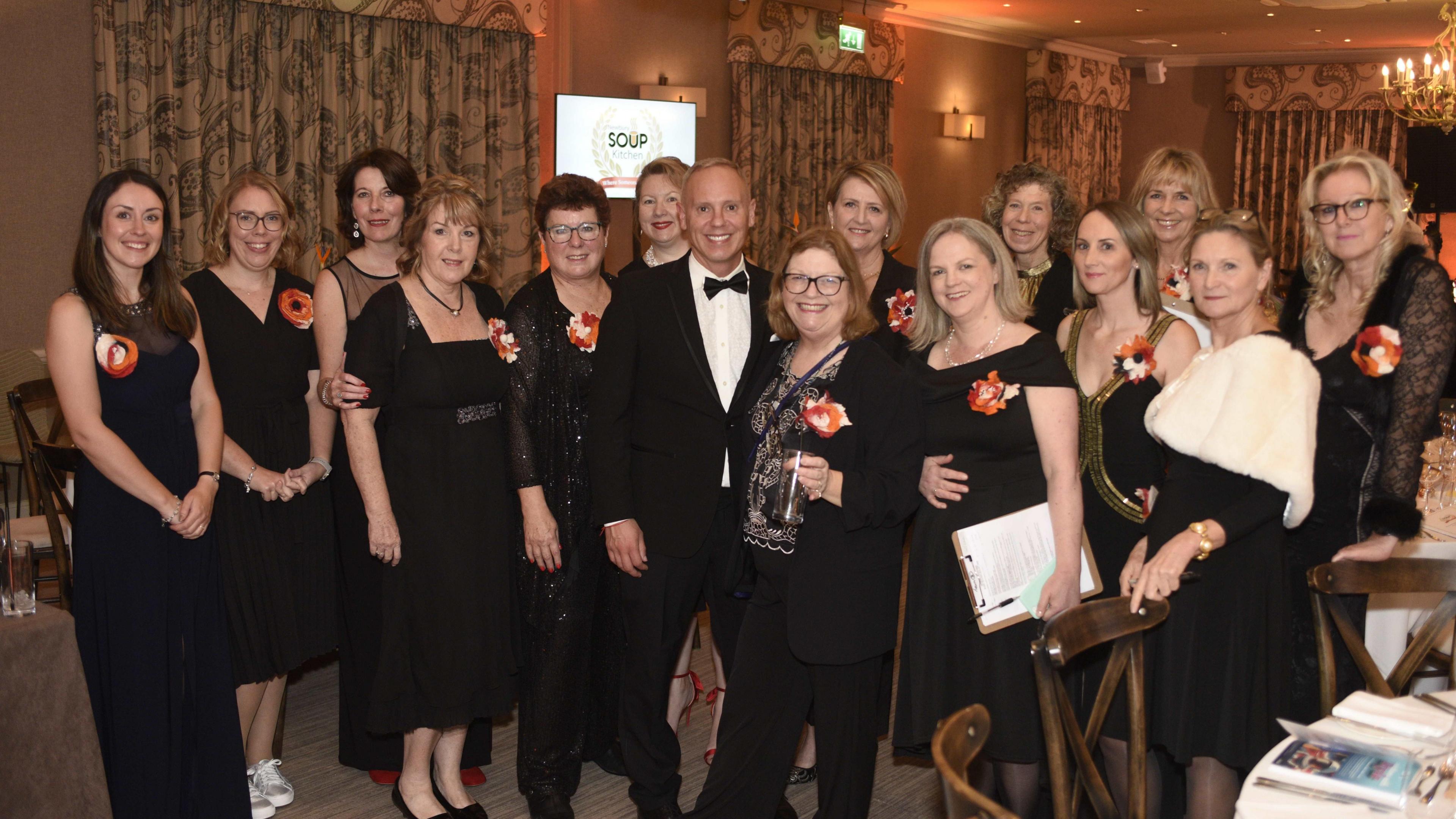 CEO and founder Meryl Praill, third on the left, is smiling with a team all dressed in evening attire.