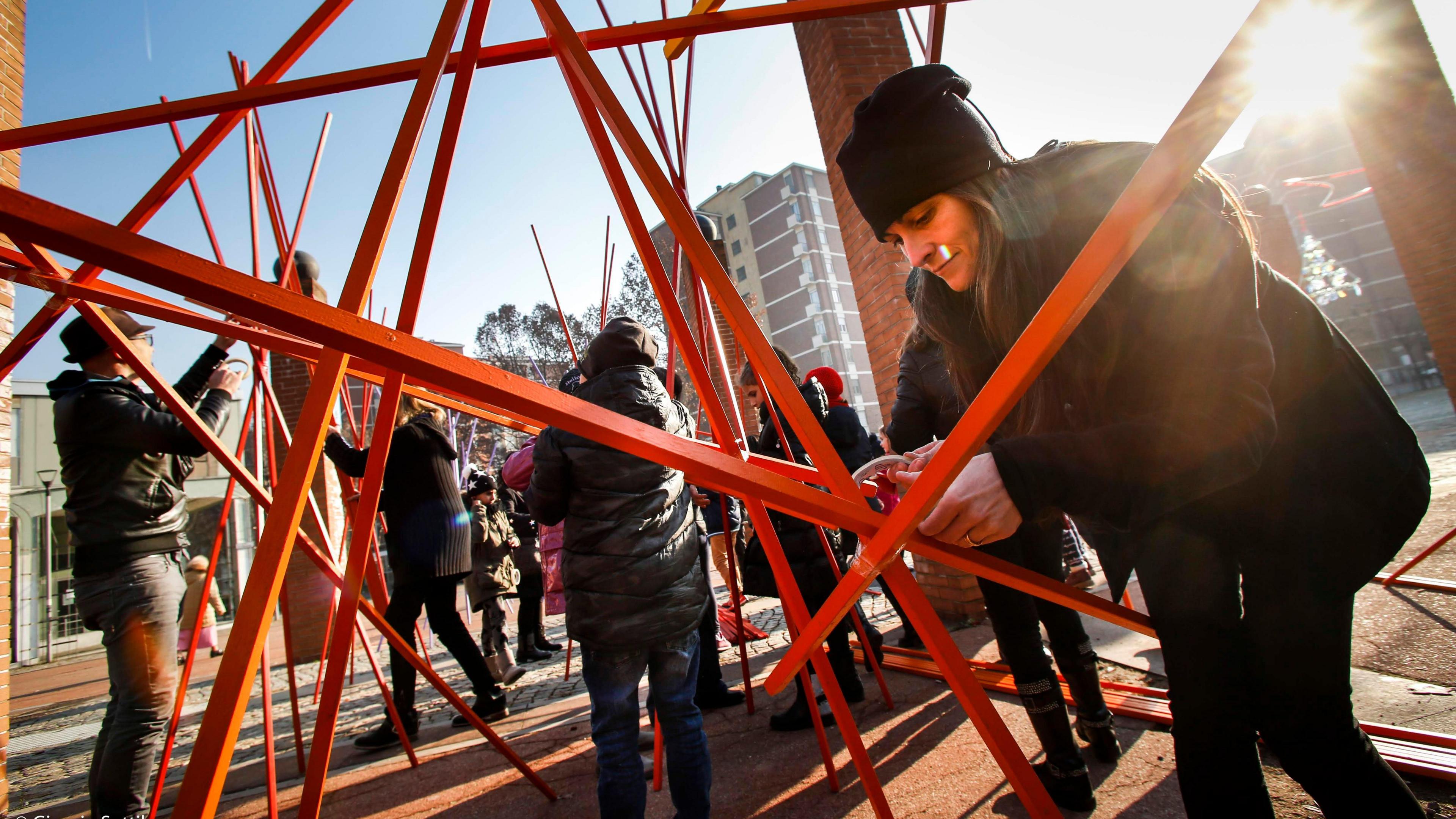 People are using lots of brightly coloured wooden sticks to create structures in a town square