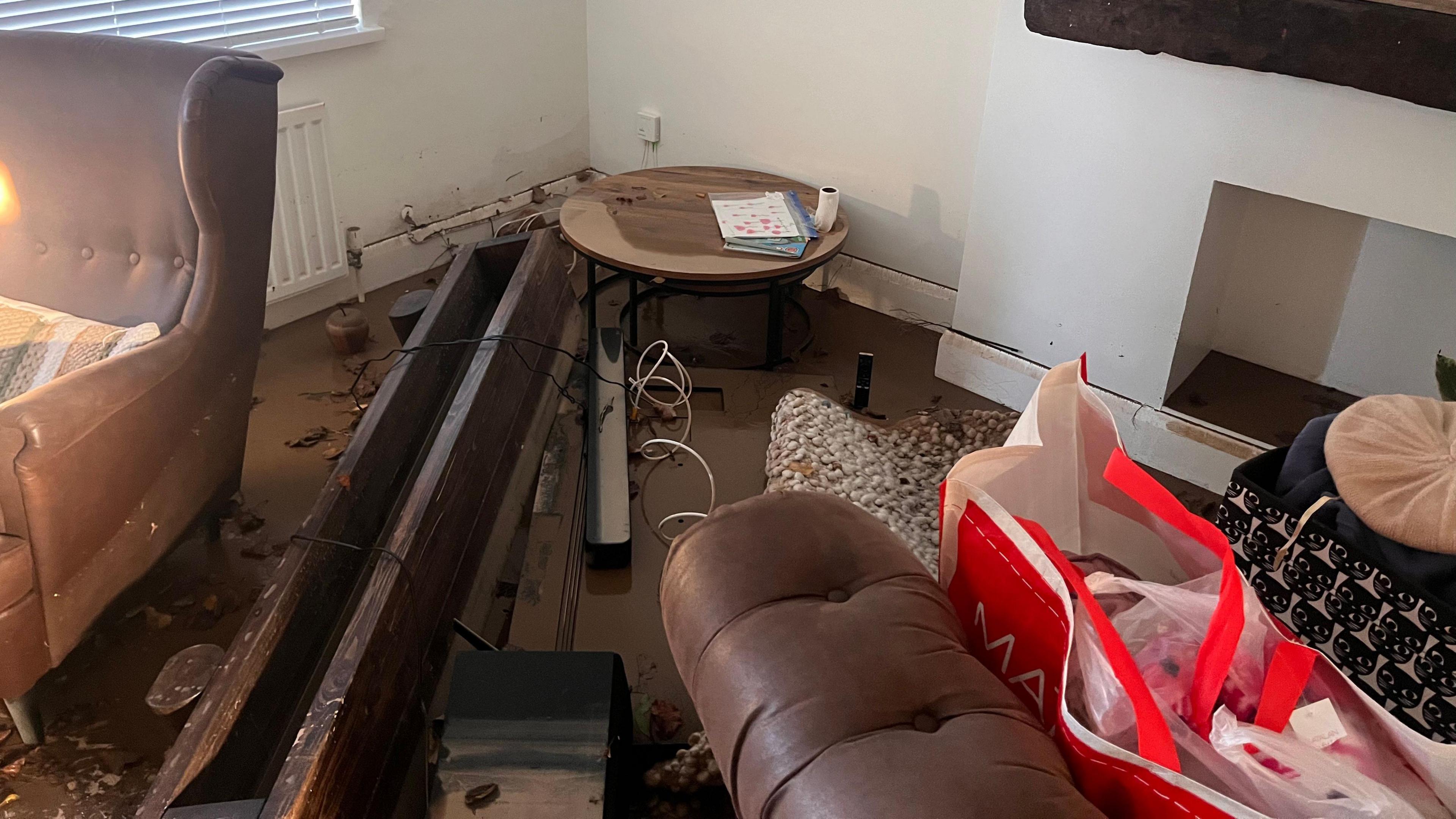 A landscape photo of damage caused to Mehdi Mozadeh's house in Dundonald following flooding. There is some water on the floor, with a coffee table pushed to the corner and a suite of brown suede furniture.