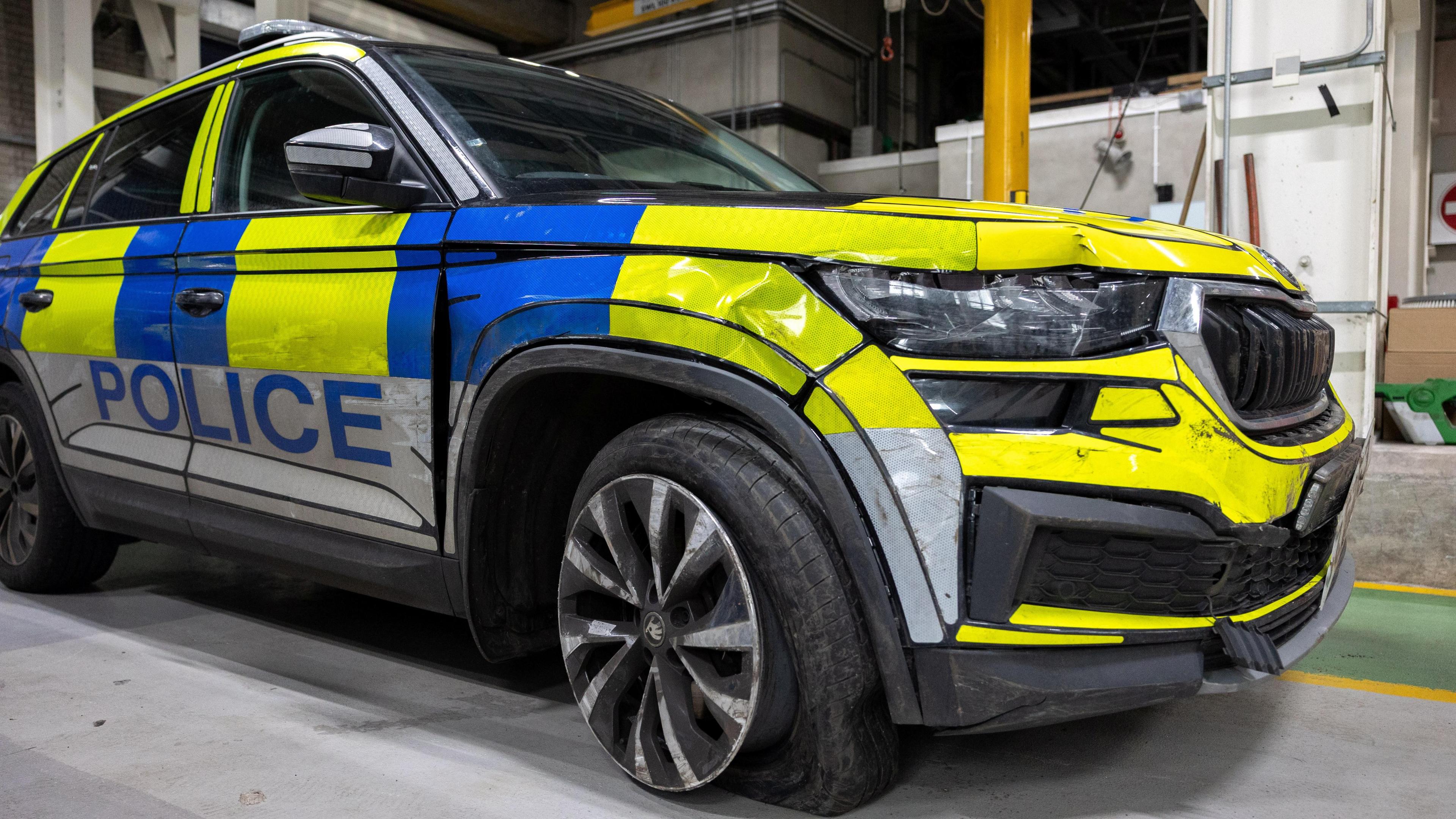 A PSNI car is damaged. The car is blue and yellow. The word police is printed on the said.
