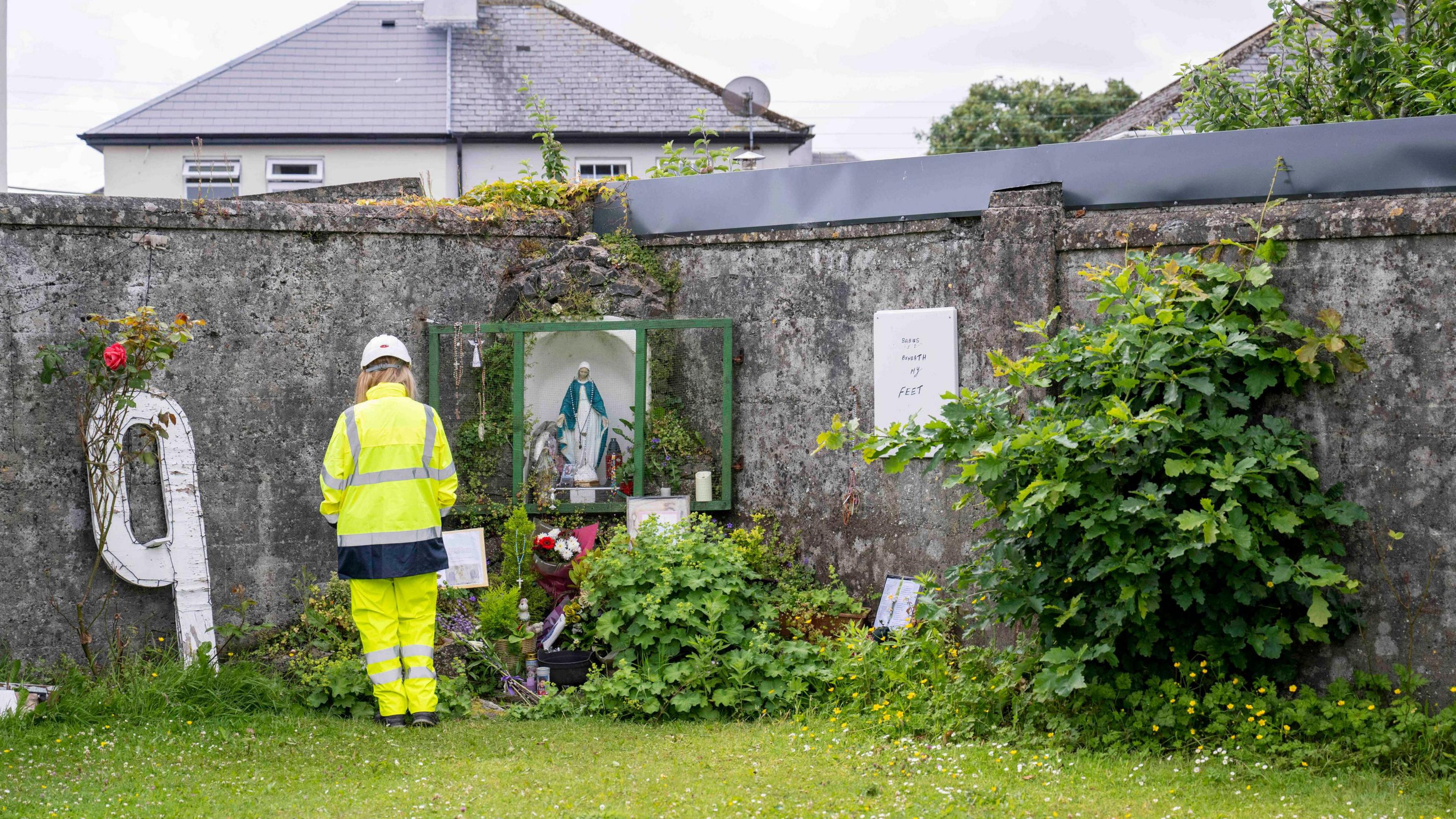 A worker in yellow high visibility clothing at a memorial left at the site of the former Mother and Baby Institution in Tuam, County Galway.