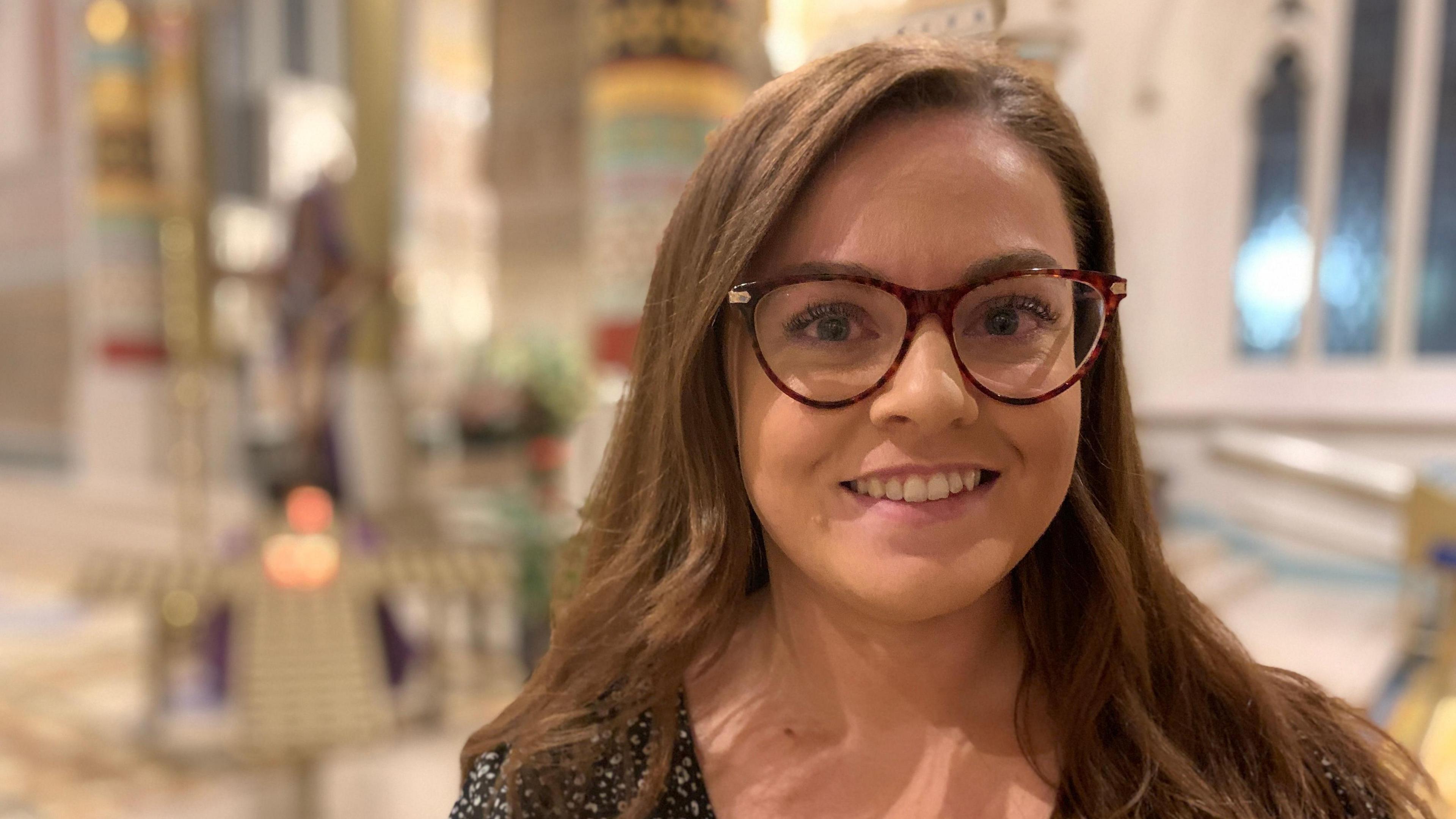 Rebecca Morris looking at the camera. She is smiling and has shoulder-length mid-brown hair and brown-rimmed glasses.