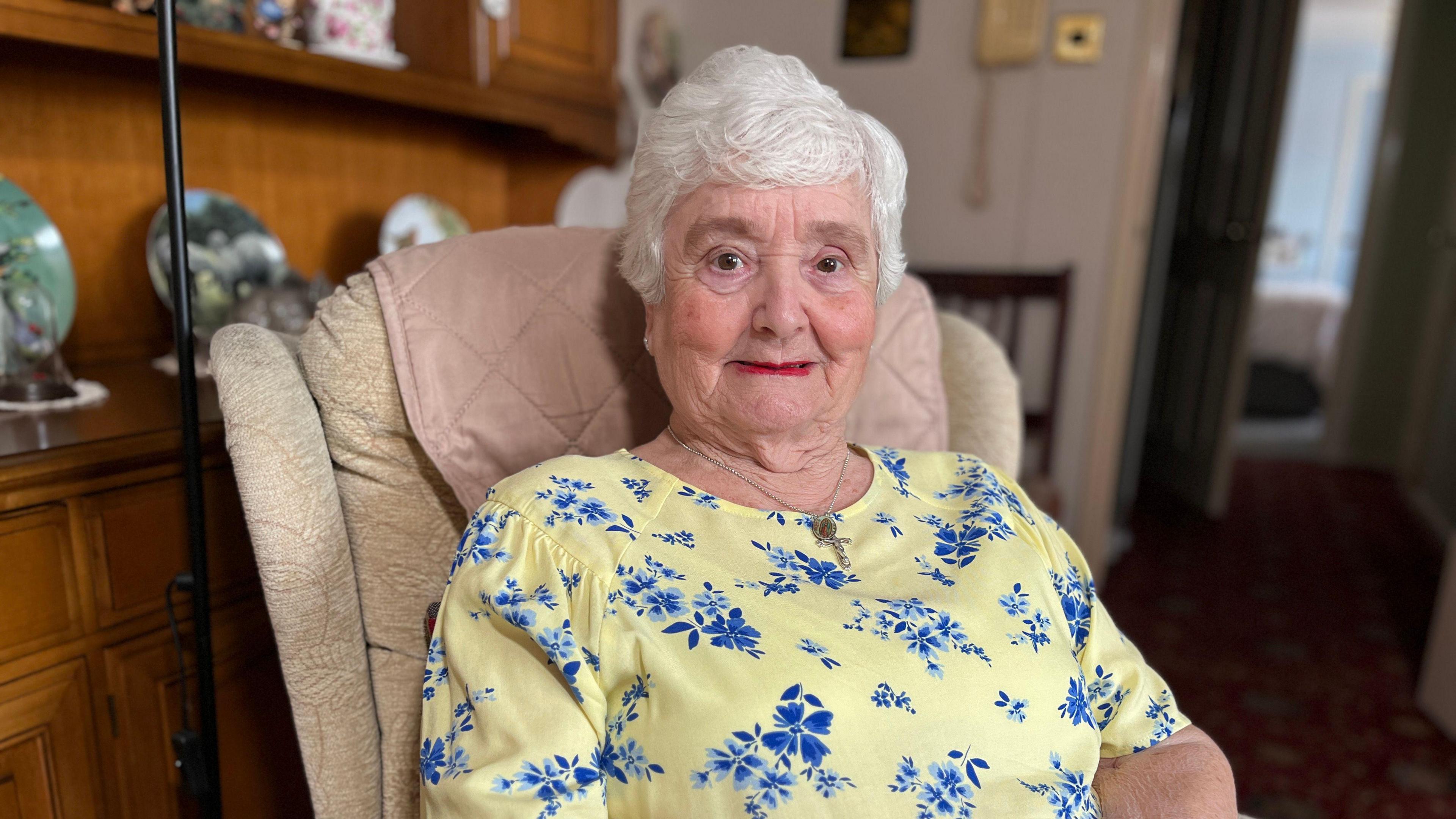 An older lady, dressed in yellow, smiles at the camera