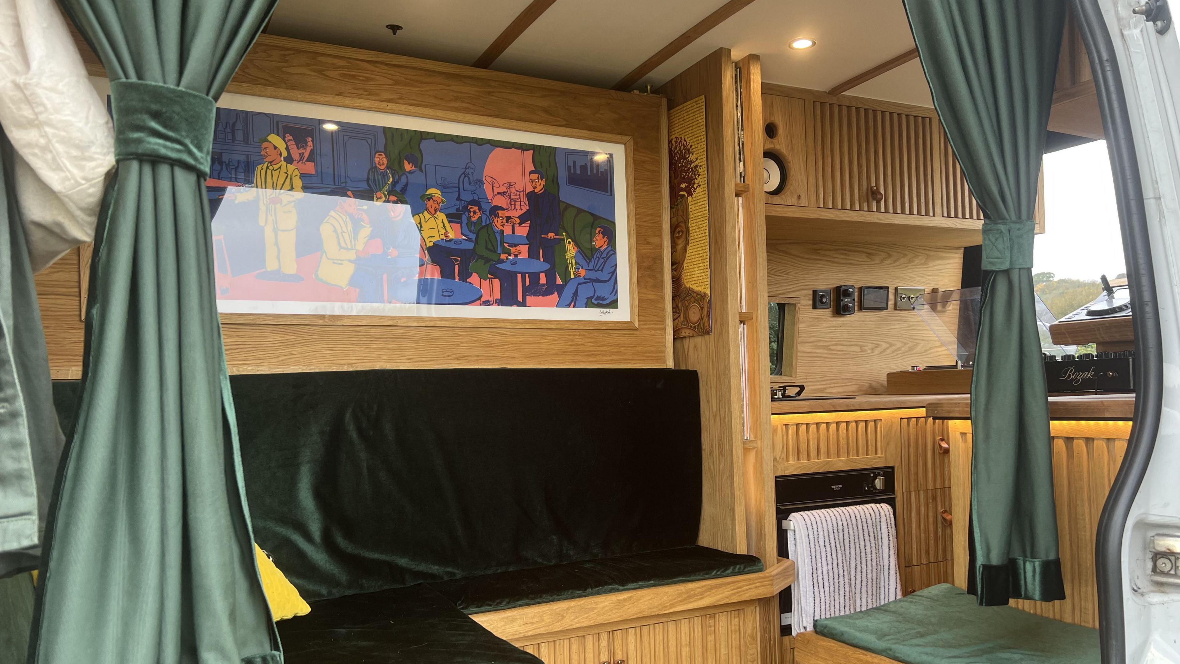 The inside of the van showing the Japanese-inspired wooden slats covering much of the cabinetry. There is a seated area with a graphic above it, and there are small green curtains tied together which separates the different living spaces. 