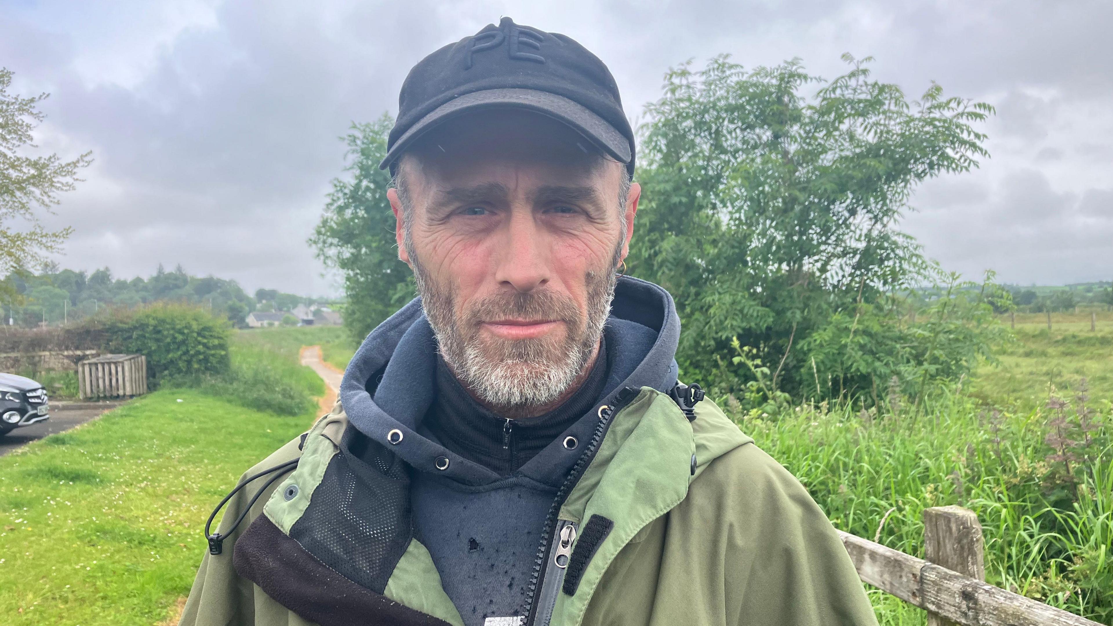 Man with a beard wearing a cap and green waterproof coat 