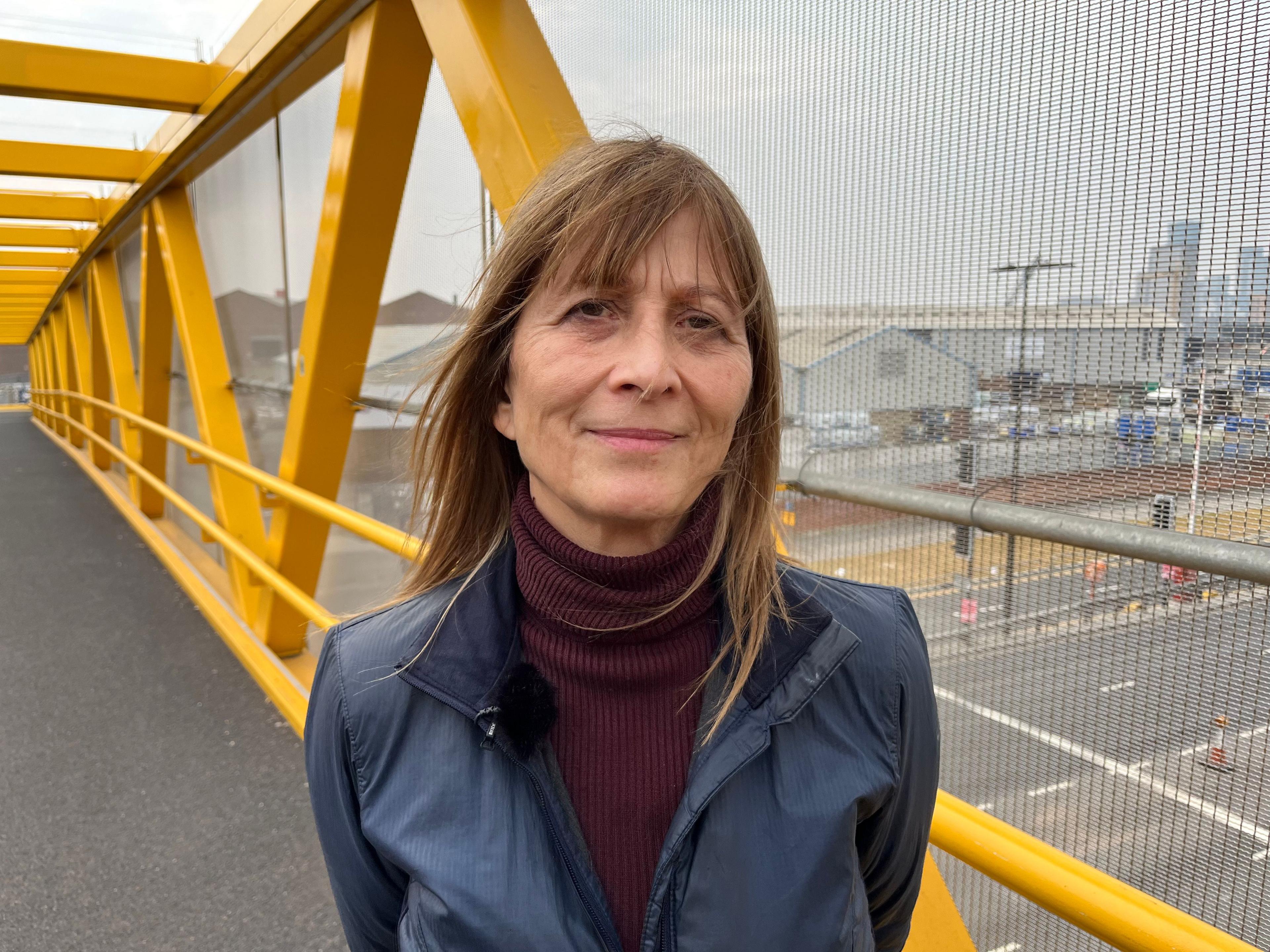 A woman stands on a yellow bridge over a road