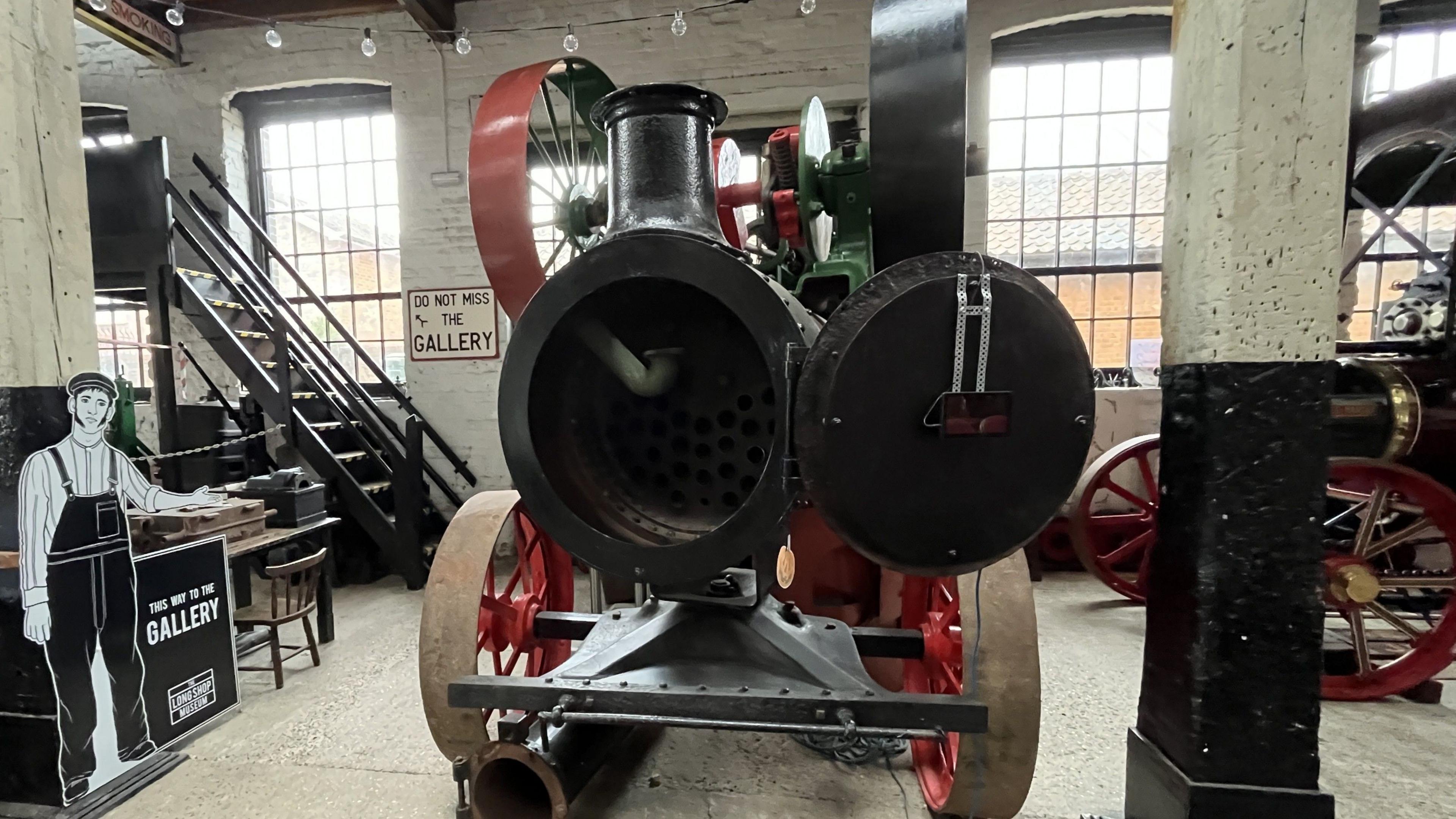 A steam engine rests inside the museum. Its circular front has been opened up revealing parts of its interior. 