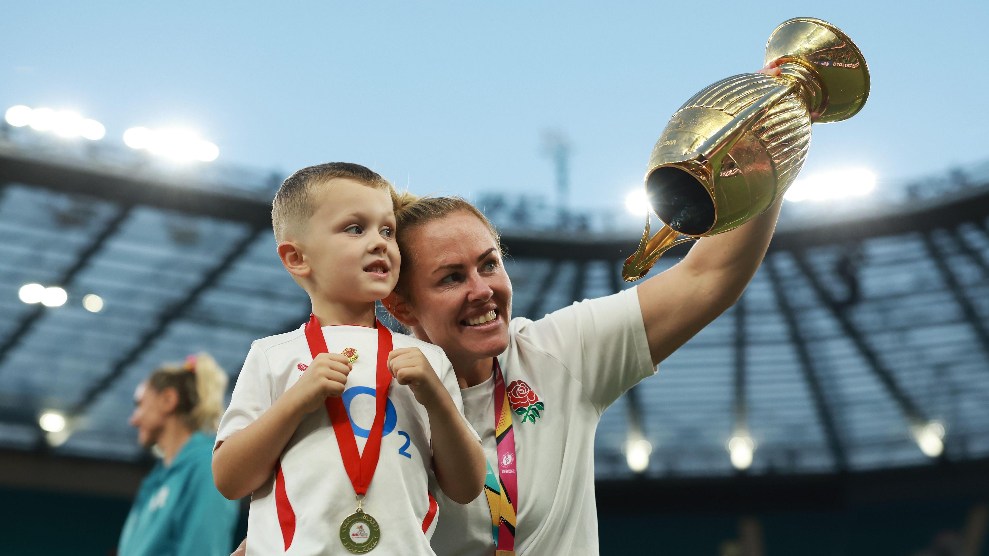 Marlie Packer holds the World Cup trophy in the air with her son Oliver next to her while on the field at Twickenham