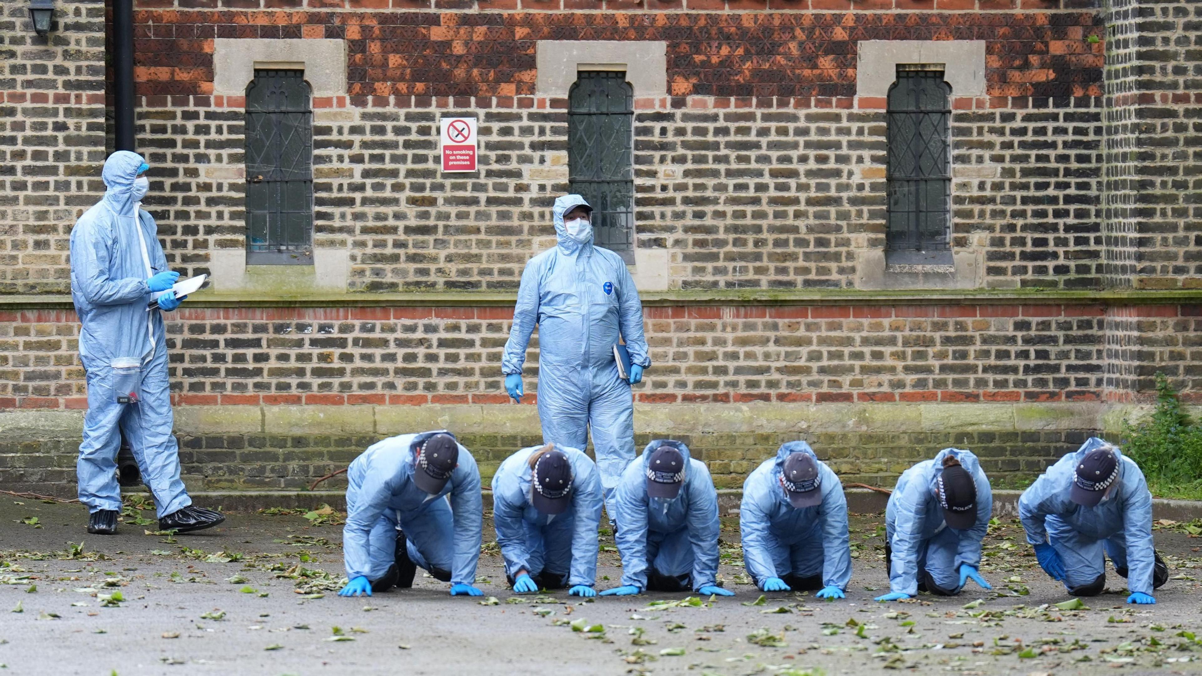 Forensic officers on all-fours carrying out search outside church in Hackney