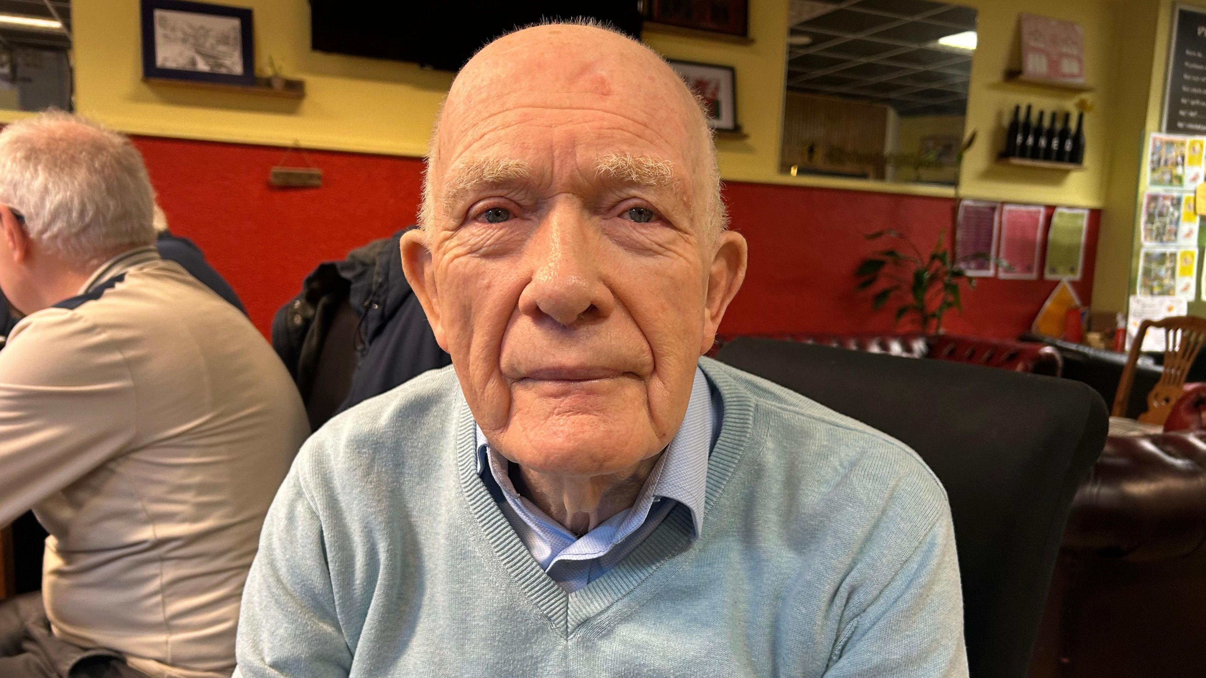 John Cullwick mewn siwmper Llwyd a chrys glas