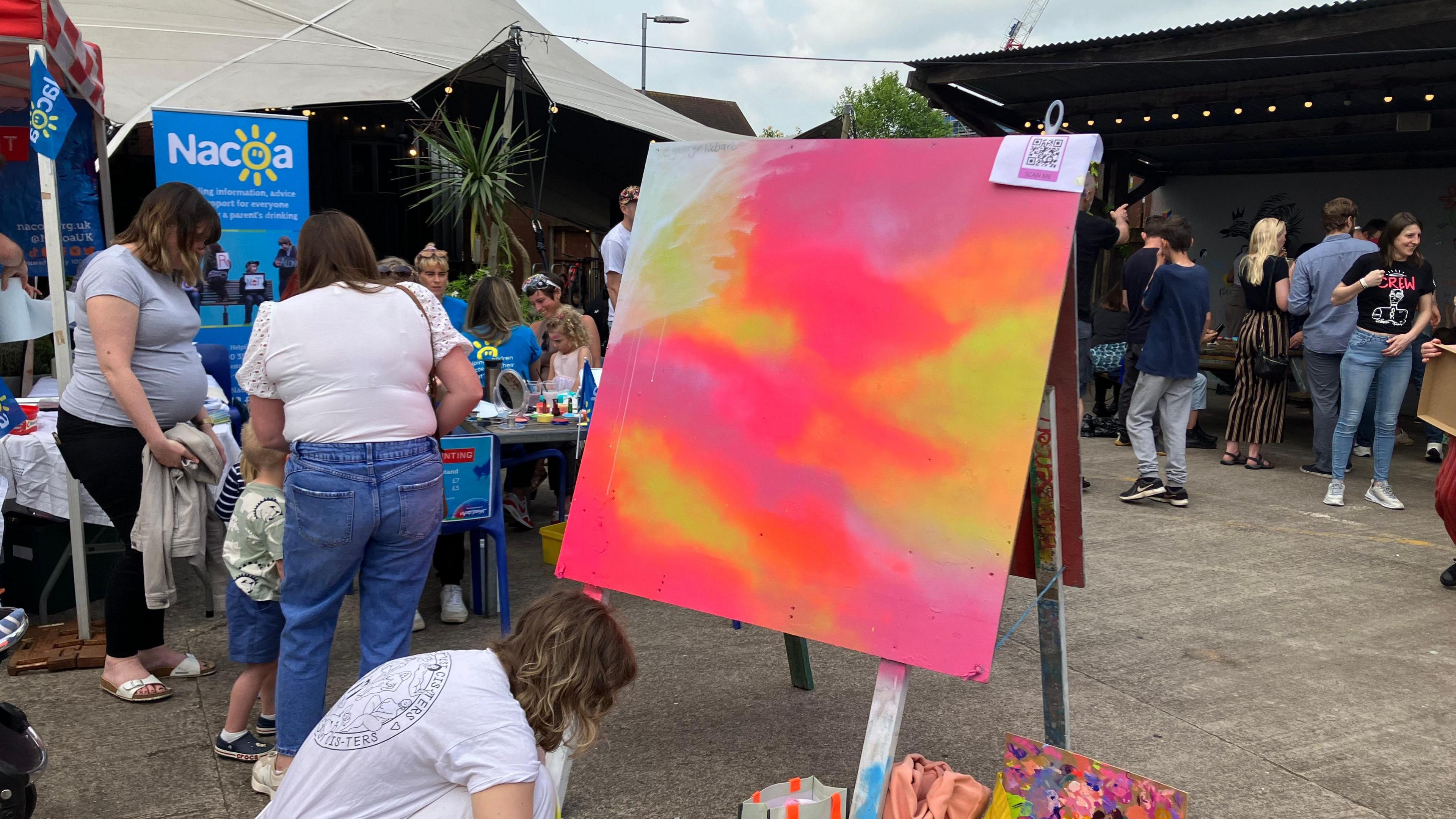 An artist crouching down in front of a painting with orange pink and yellow tones