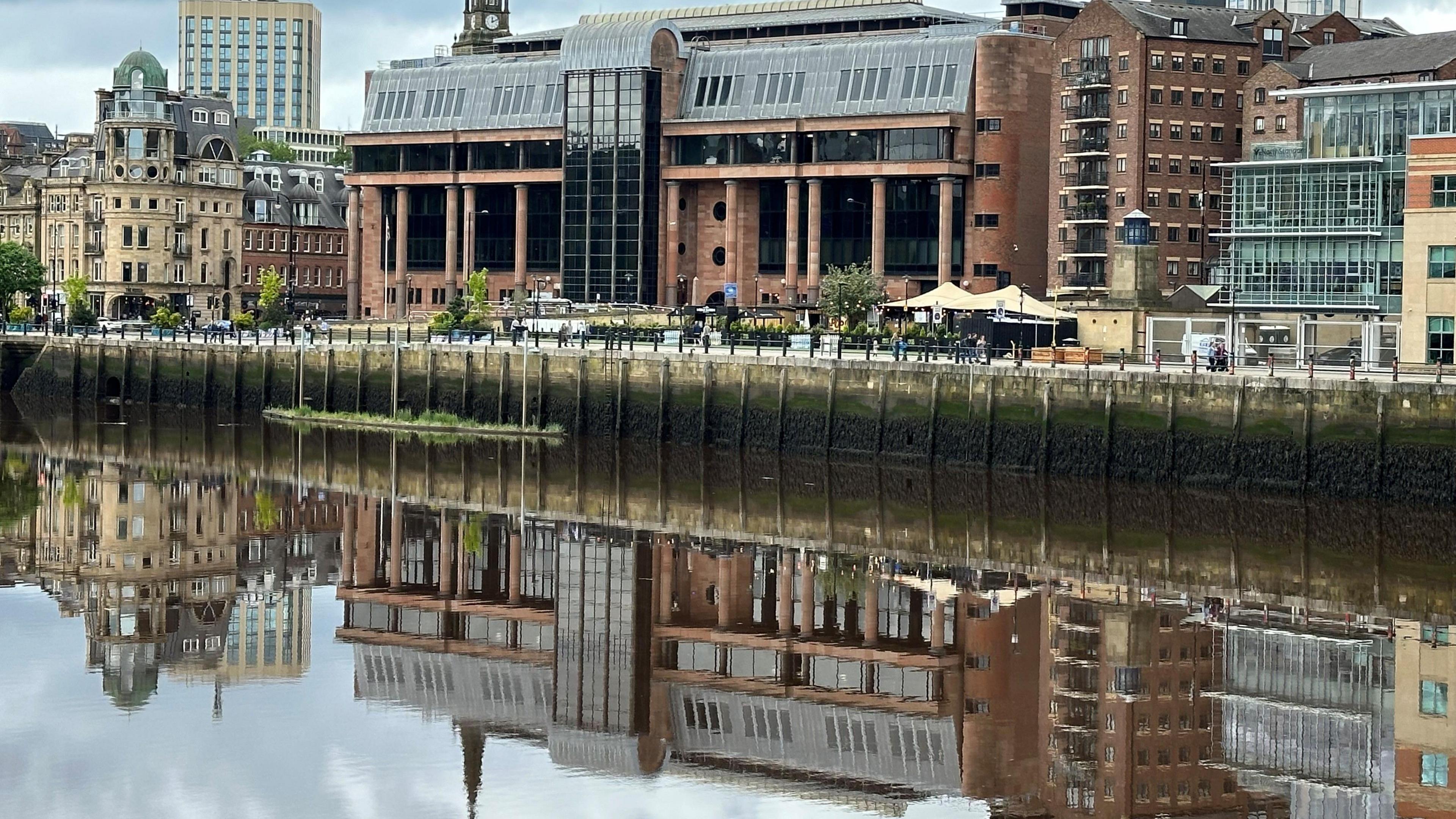 The imposing court building made of red bricks and large dark windows reflected in the river. 