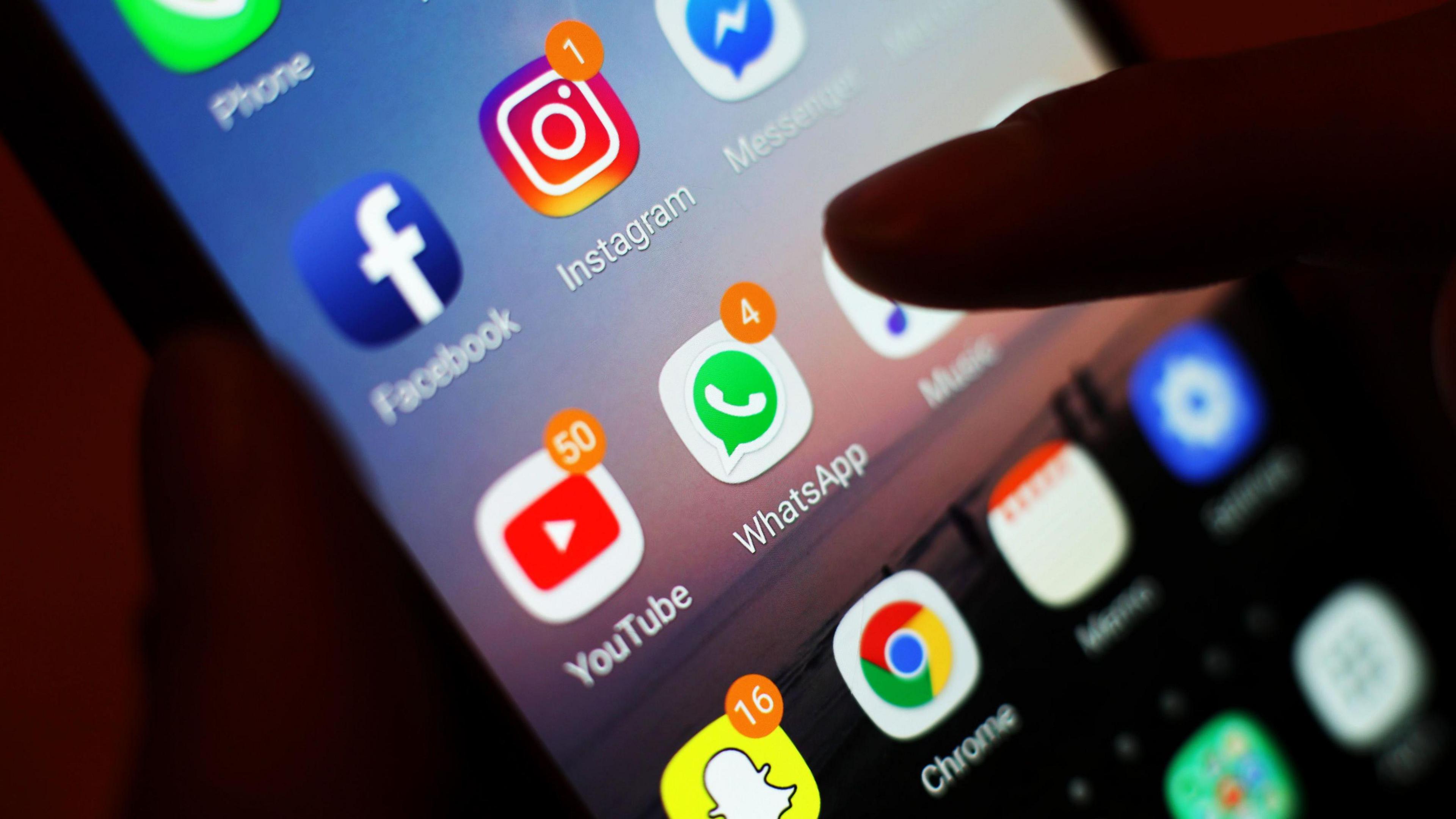 silhouette of person's finger pointing to a variety of social media apps on a smartphone