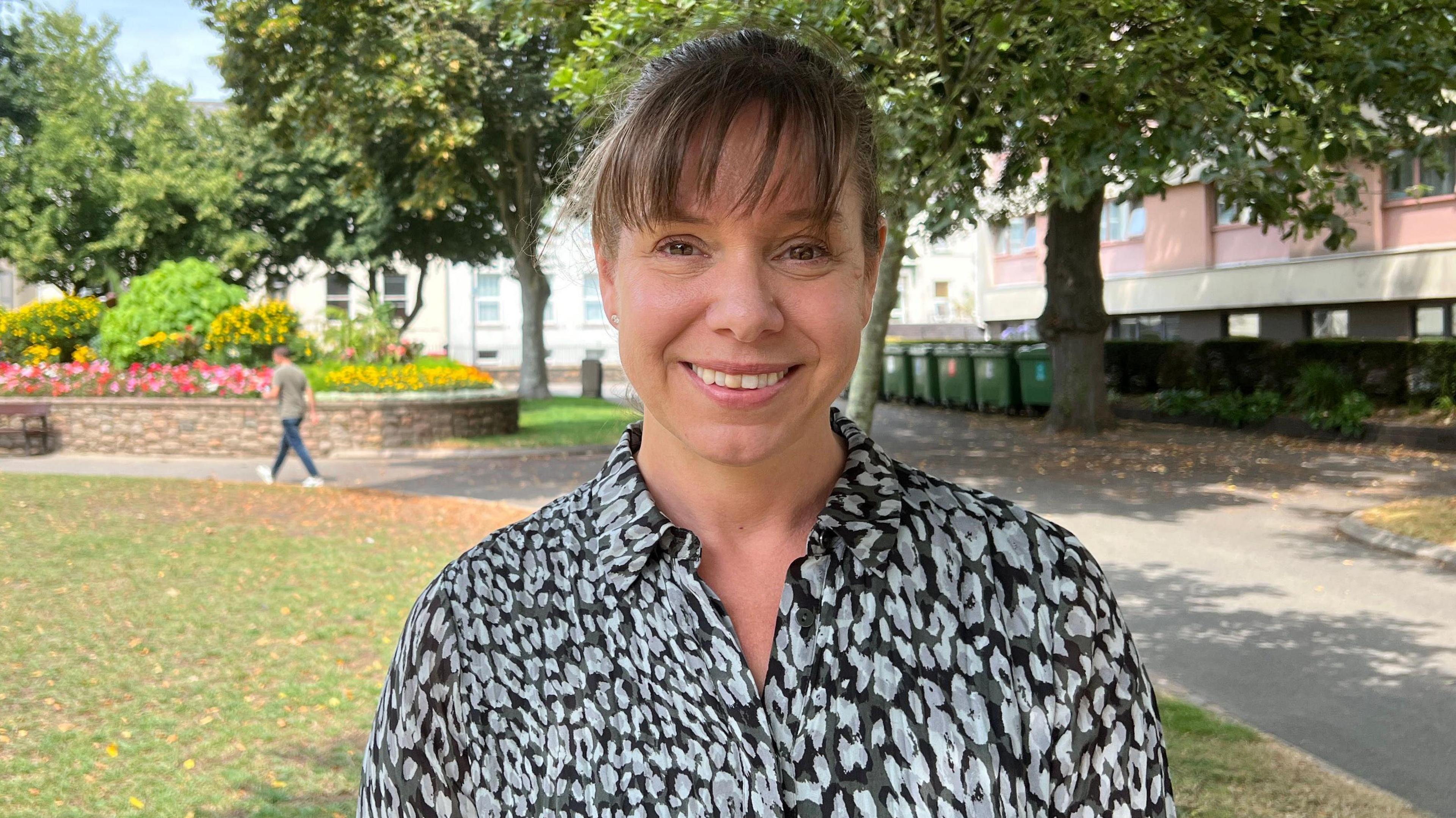 Fiona Vacher standing in a park-like area with trees, flower beds and pathways in the background.
