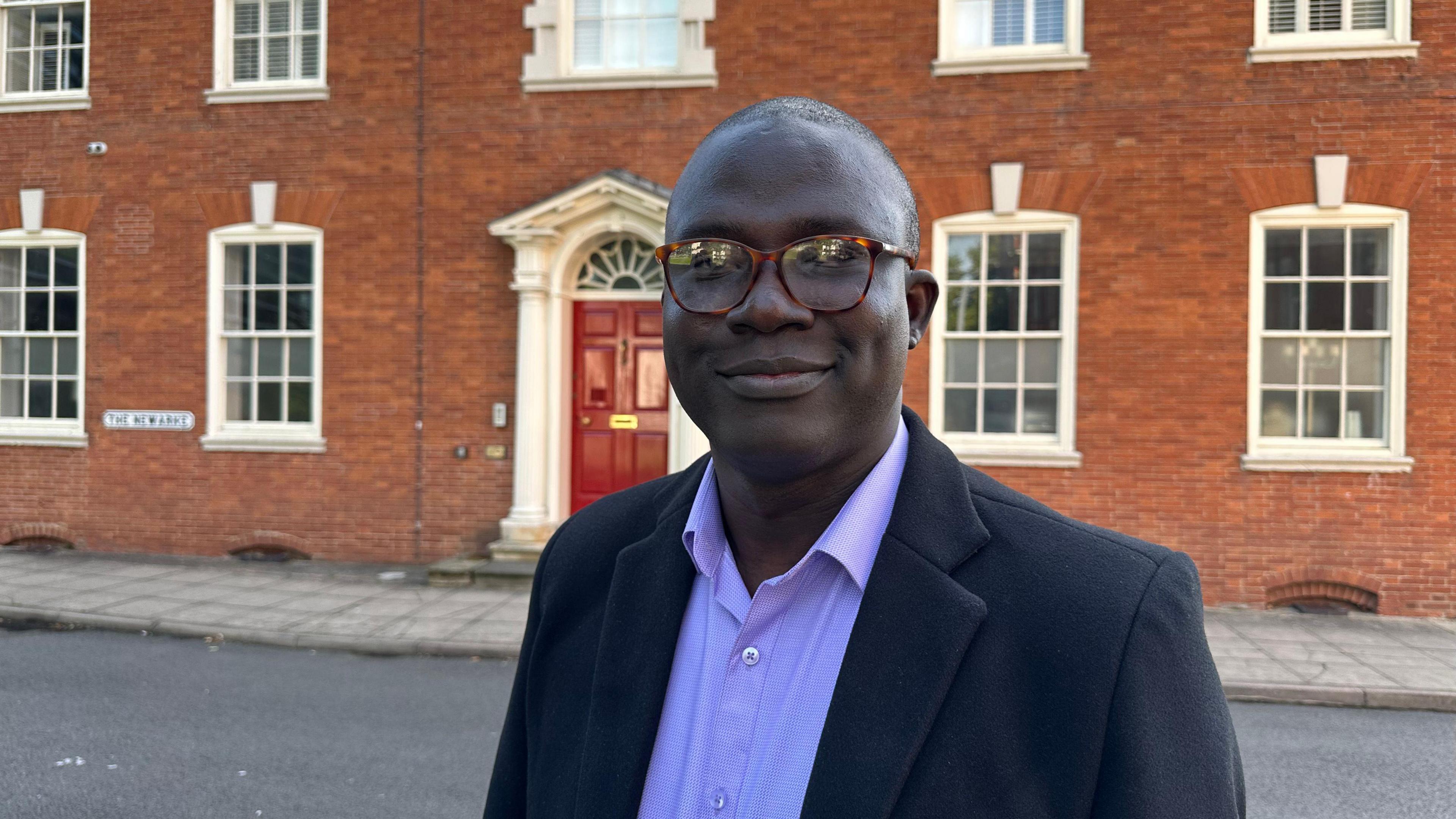 Dr Abiodun Egbetokun wearing a blue suit standing in front of a red brick building